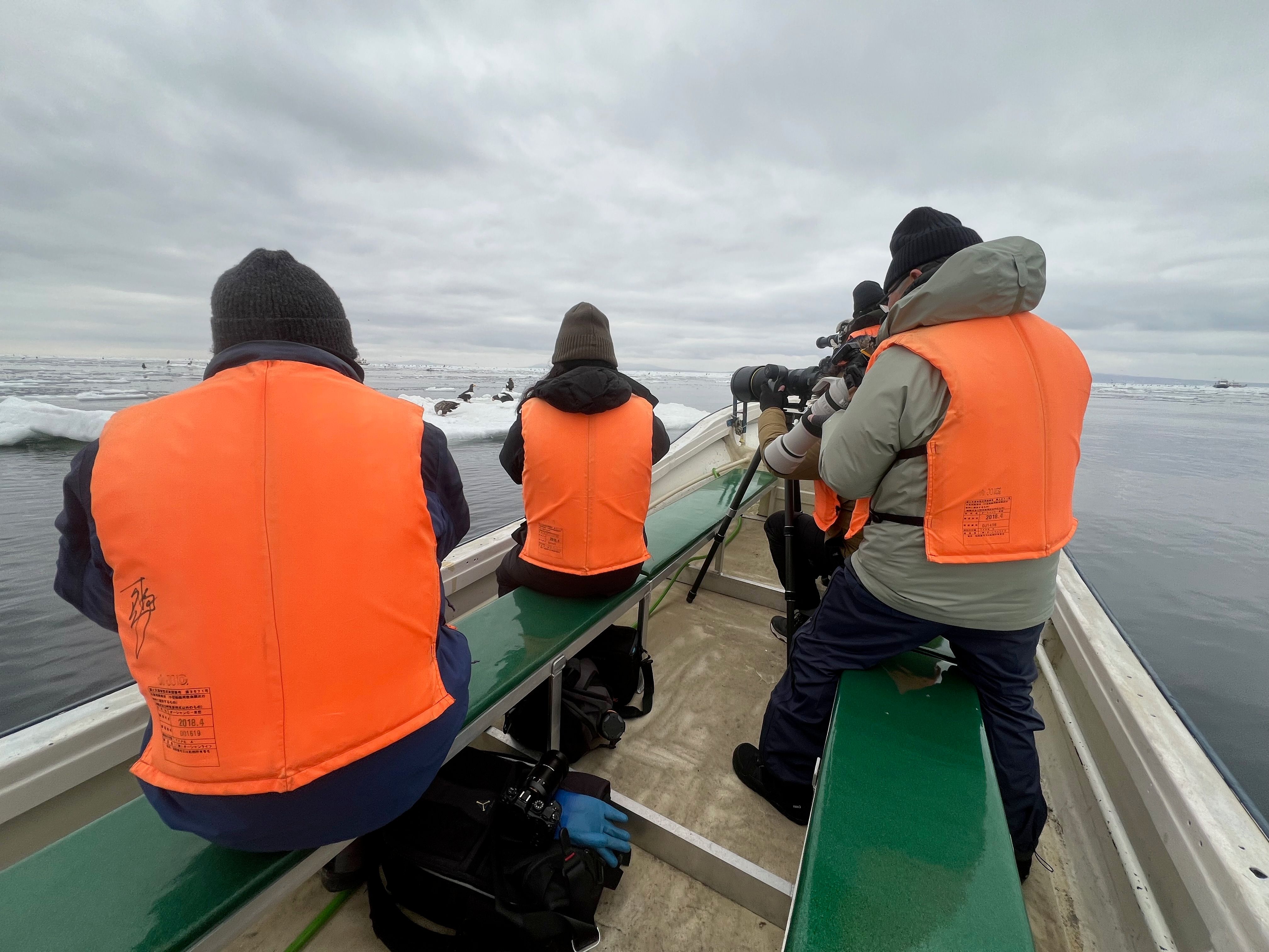 A group of photographers on a small boat. They all have their cameras out or mounted on tripods, pointed towards a group of Steller's sea eagles on an ice floe.