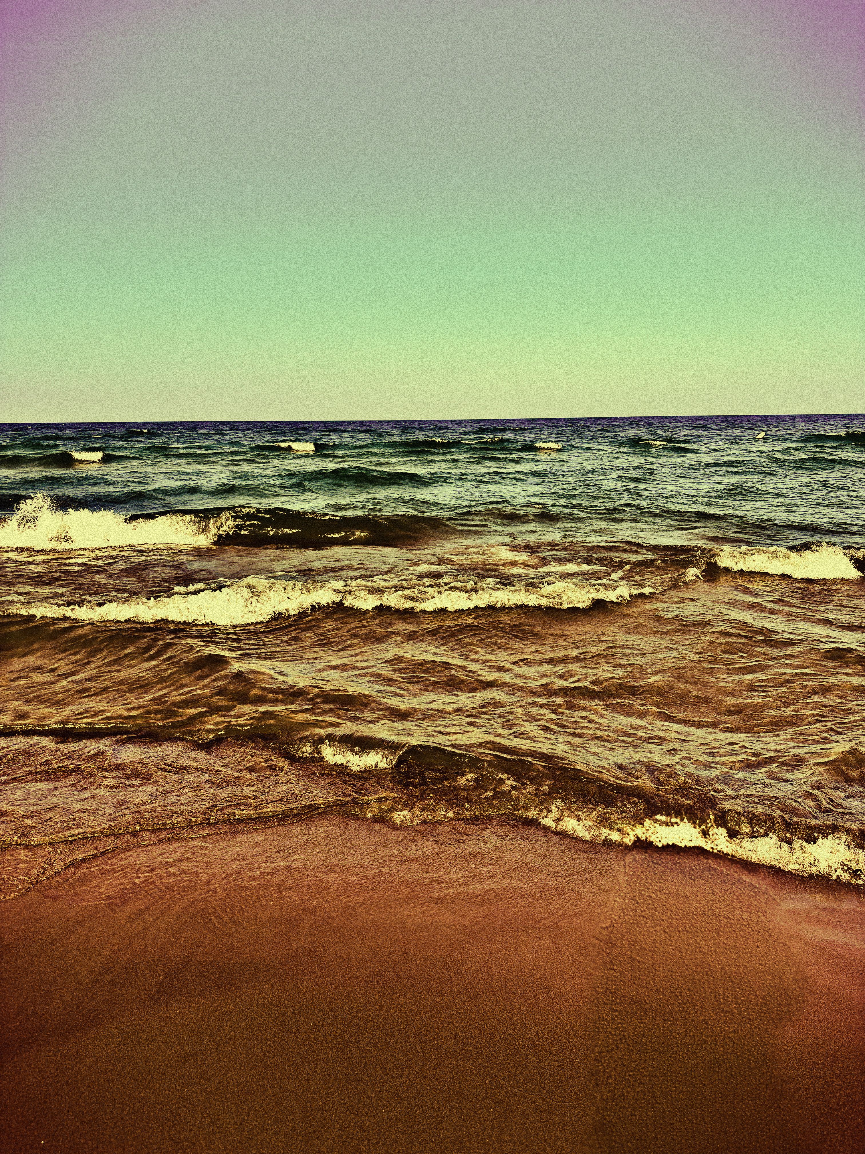 Waves rolling onto a sandy beach under a vintage-toned green and amber sky
