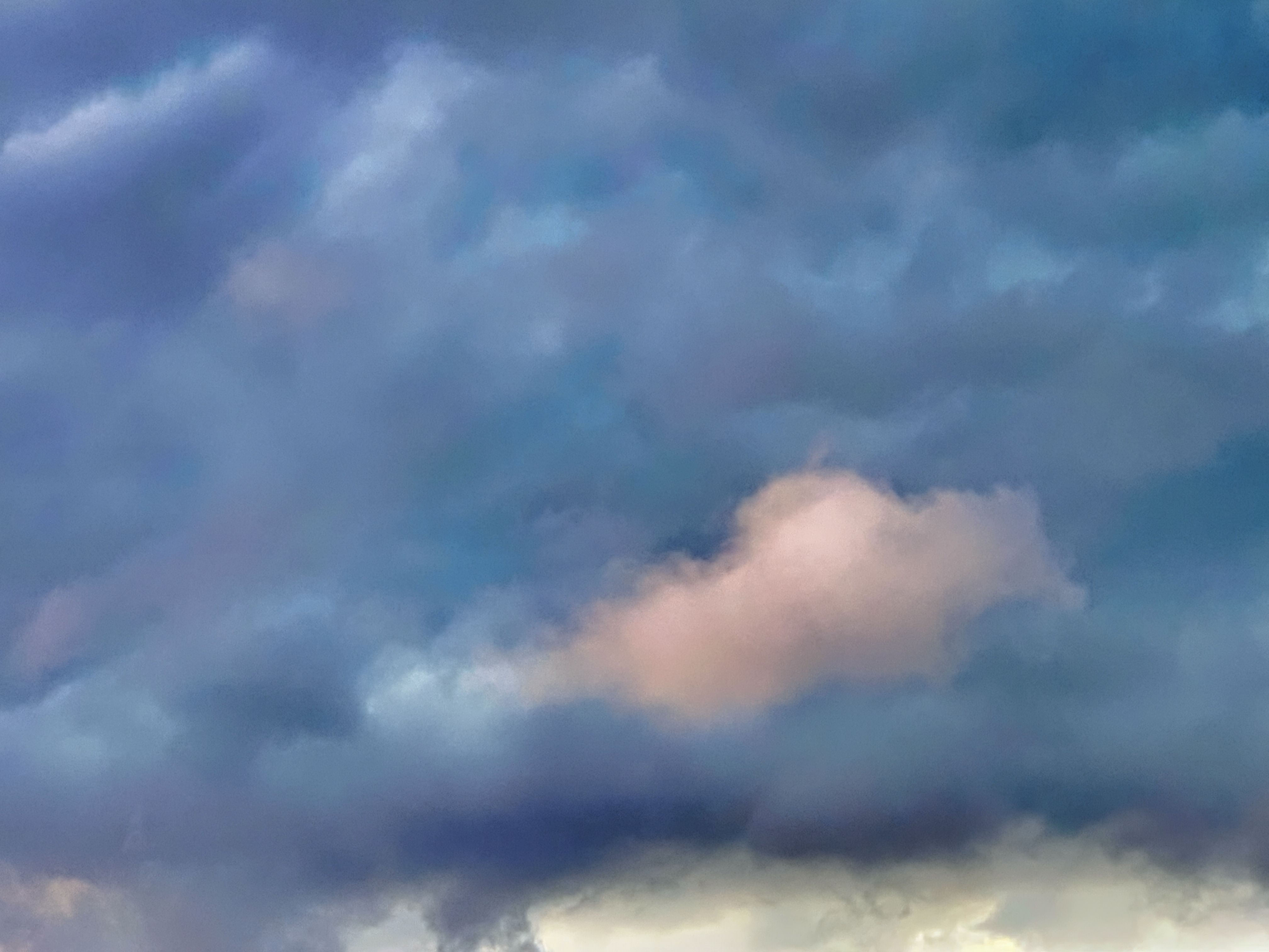 Layered storm clouds in blue-gray tones with a soft peach-pink glow breaking through