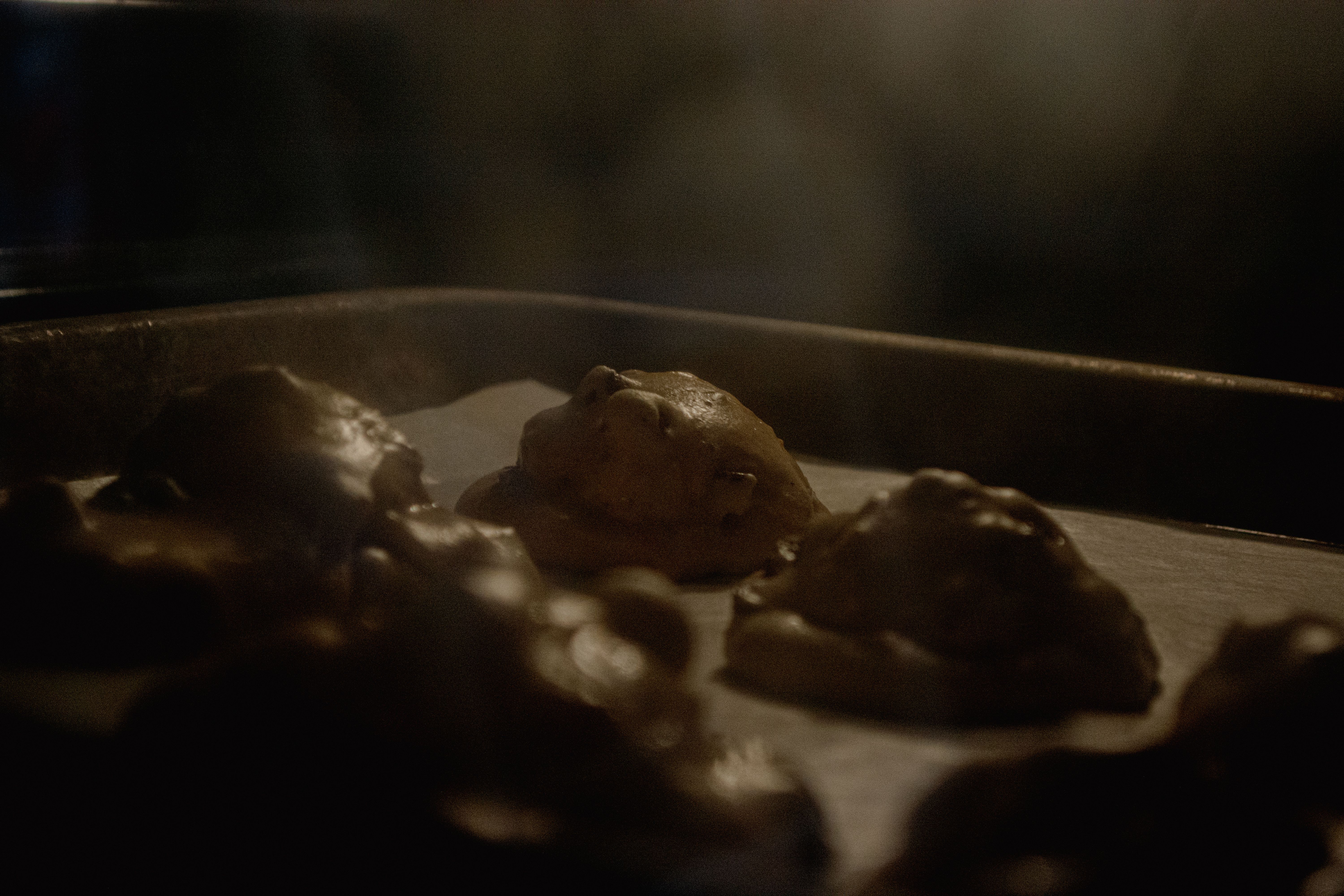 Three lumps of raw cookie dough on a baking sheet, dim warm kitchen light