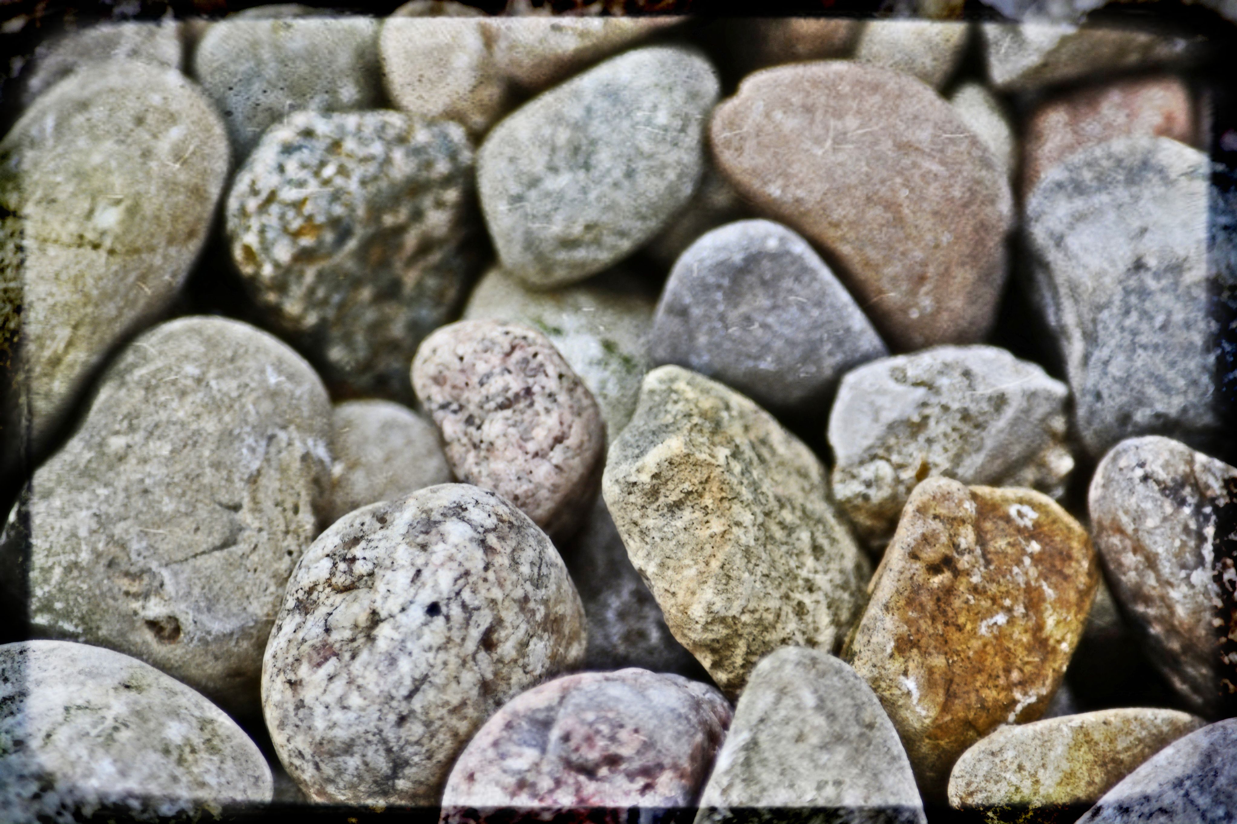 Close-up of smooth river rocks in muted earth tones, vignette-framed macro