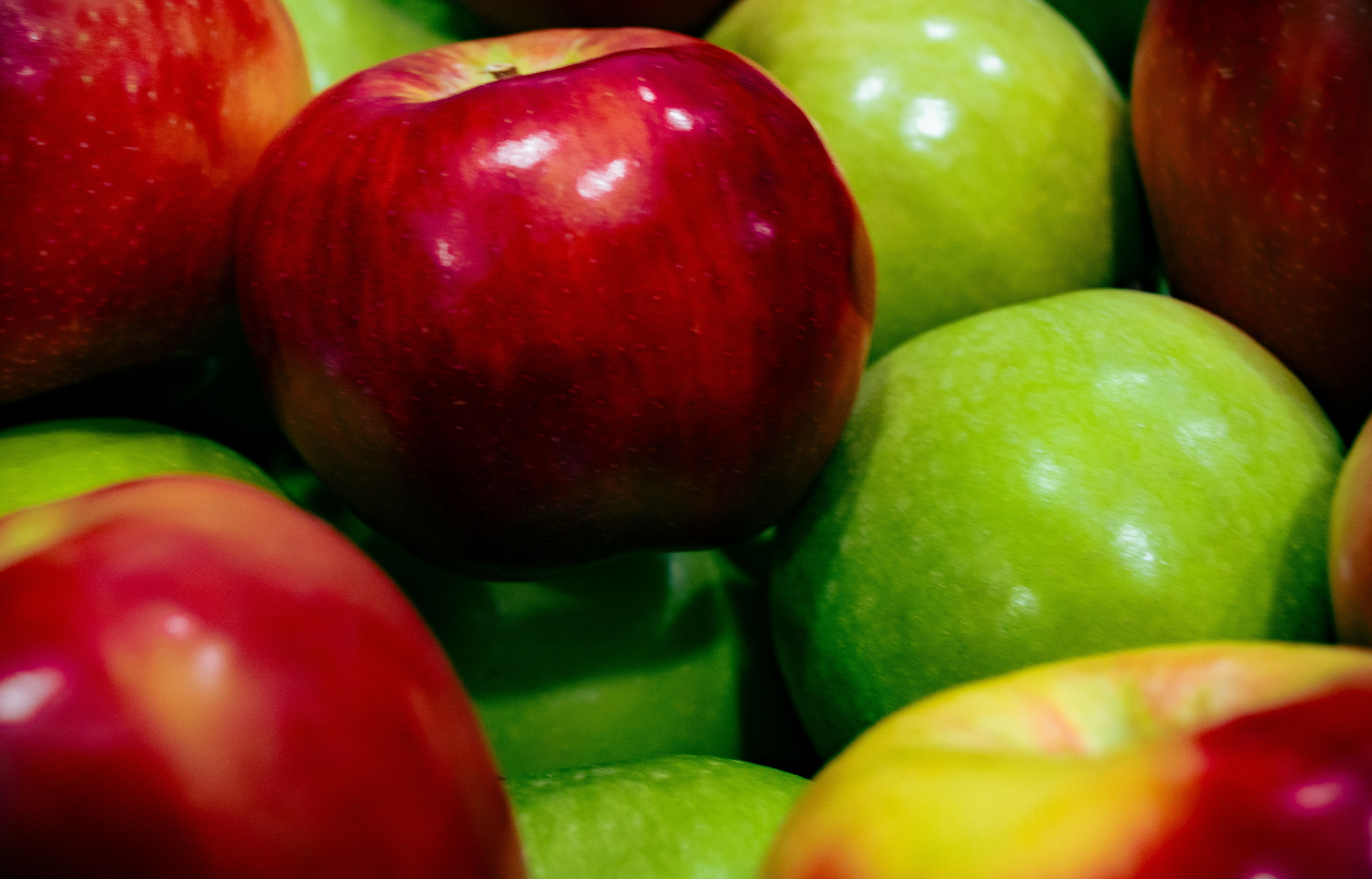 Glossy red and green apples piled close together, catching bright highlights