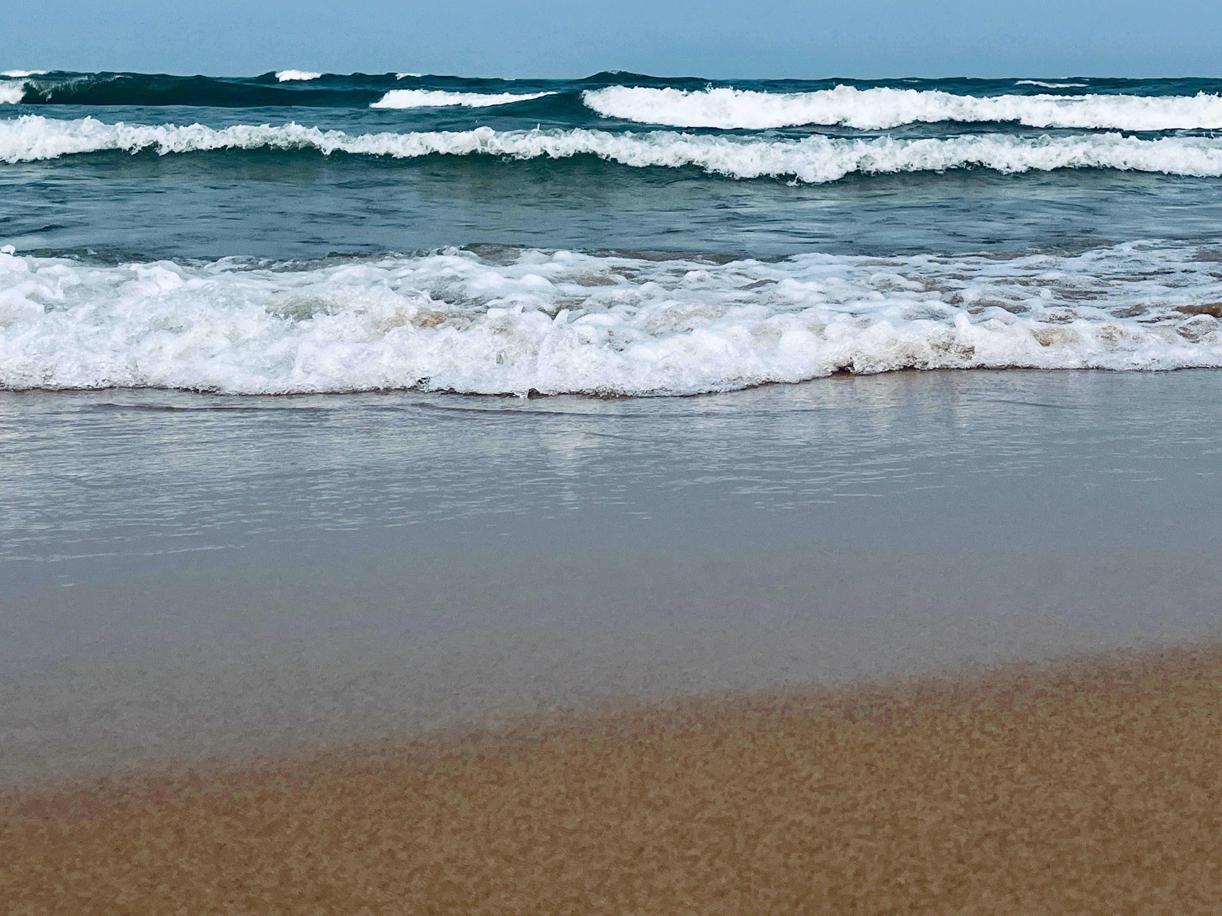 White foam waves roll onto wet tan sand under a hazy blue sky