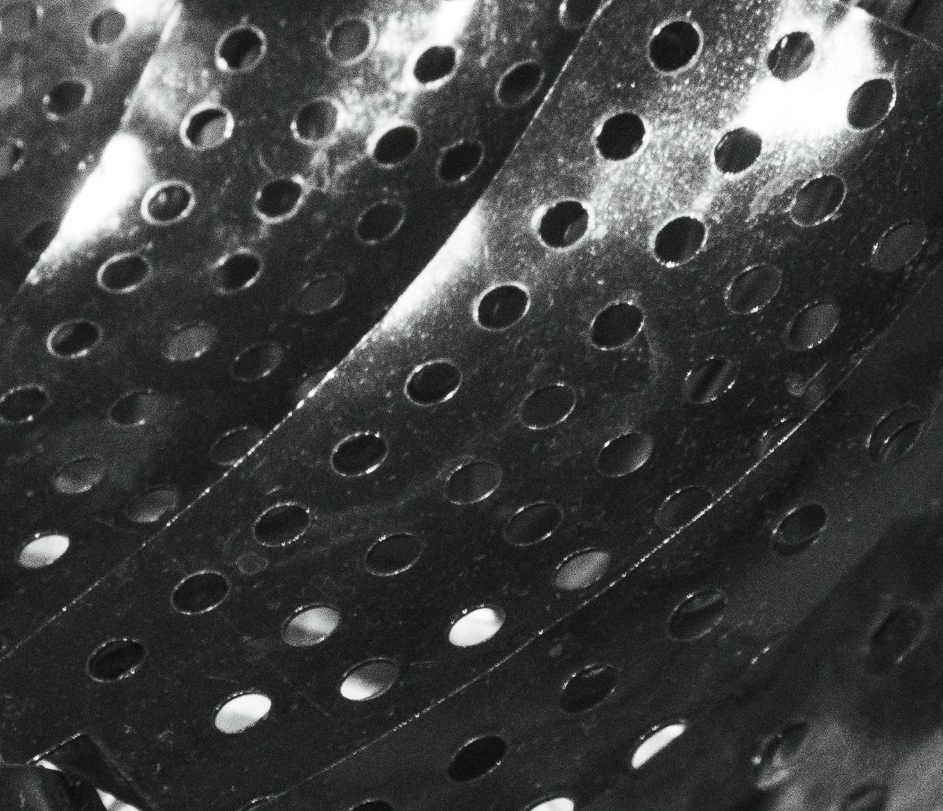 Rows of round perforations in brushed metal panels, angled with soft light