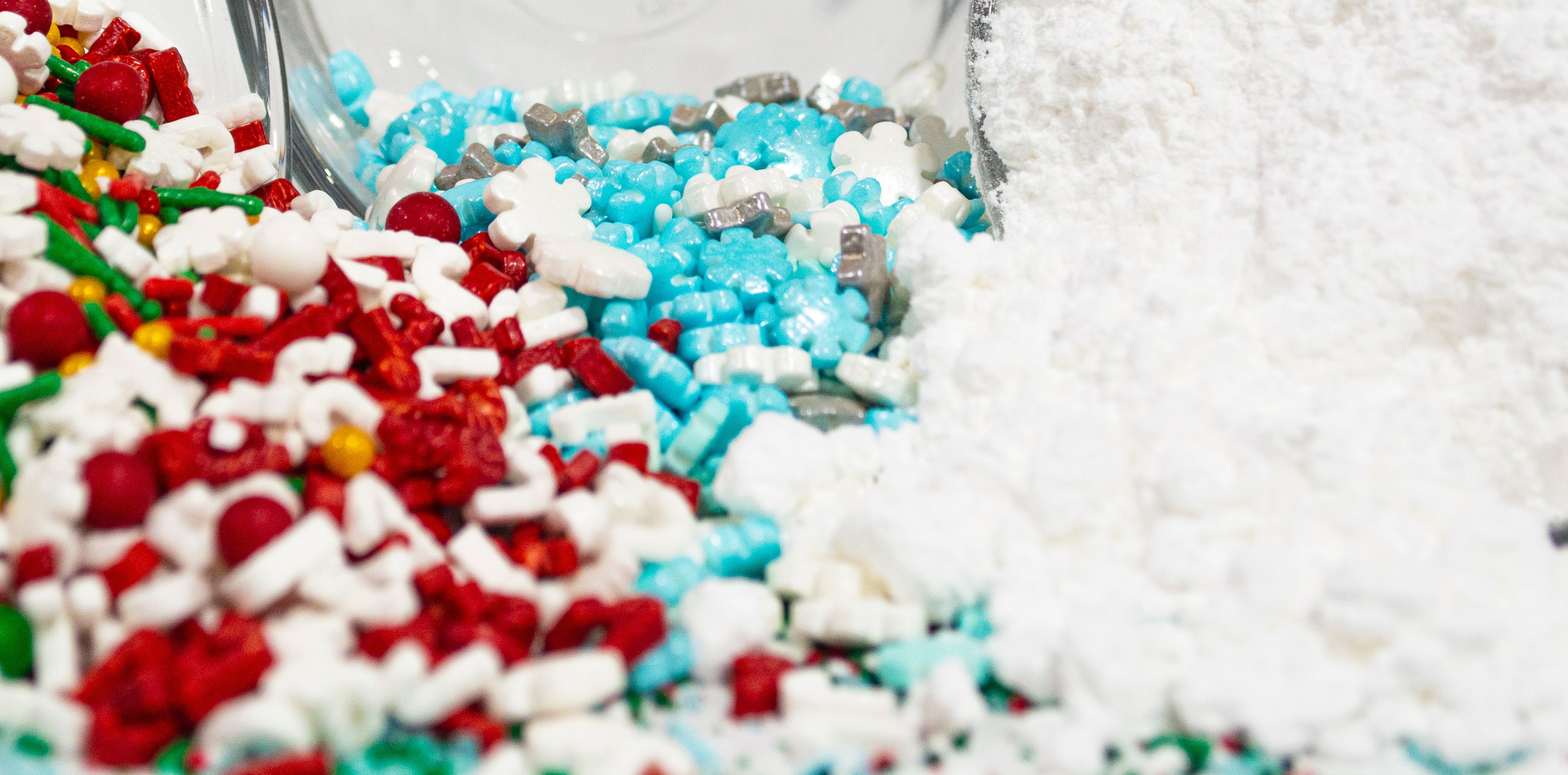Close-up of red, blue, and white candy sprinkles spilling into a mound of powdered sugar