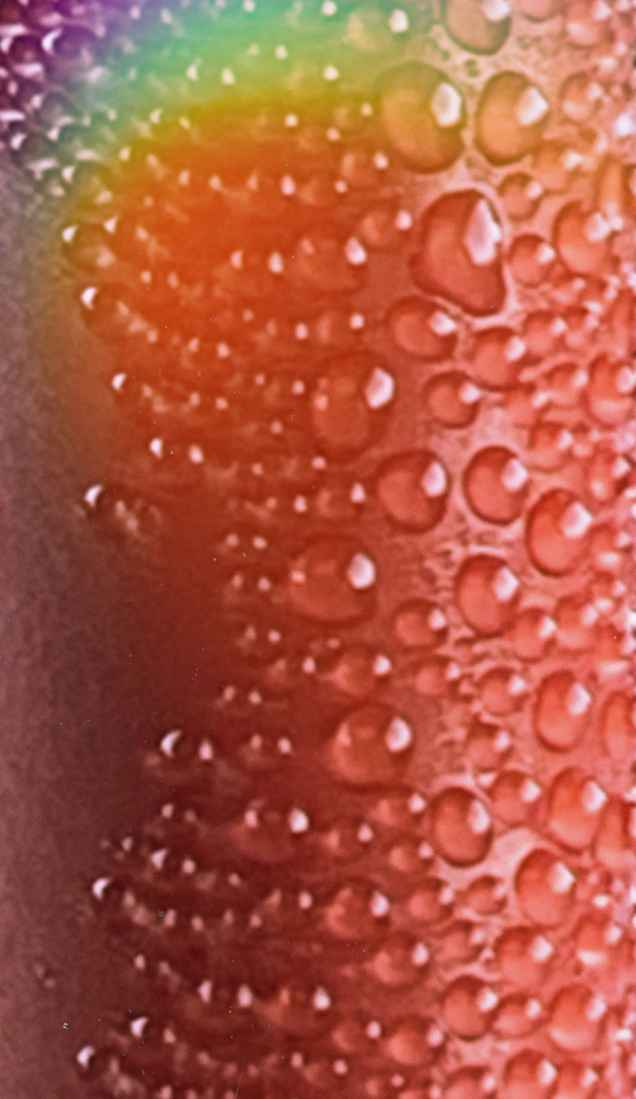 Macro water droplets on orange surface with a rainbow light flare across corner