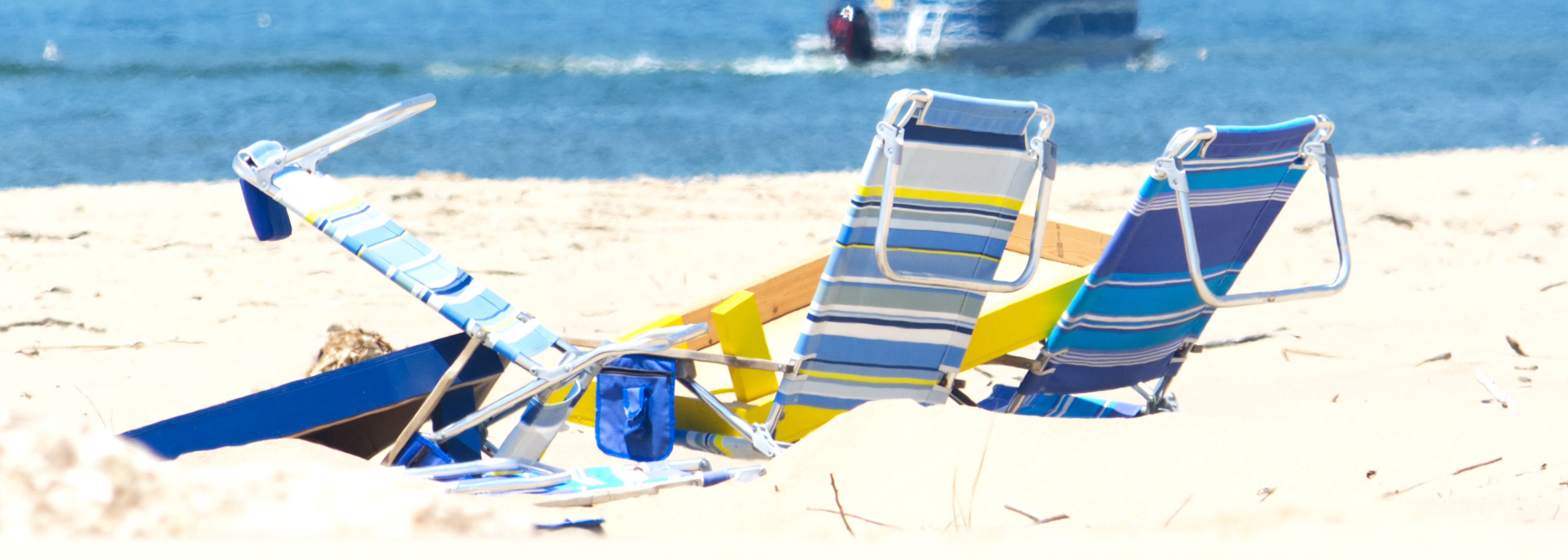 Blue-striped beach chairs and boogie boards planted in sand, a boat passing offshore