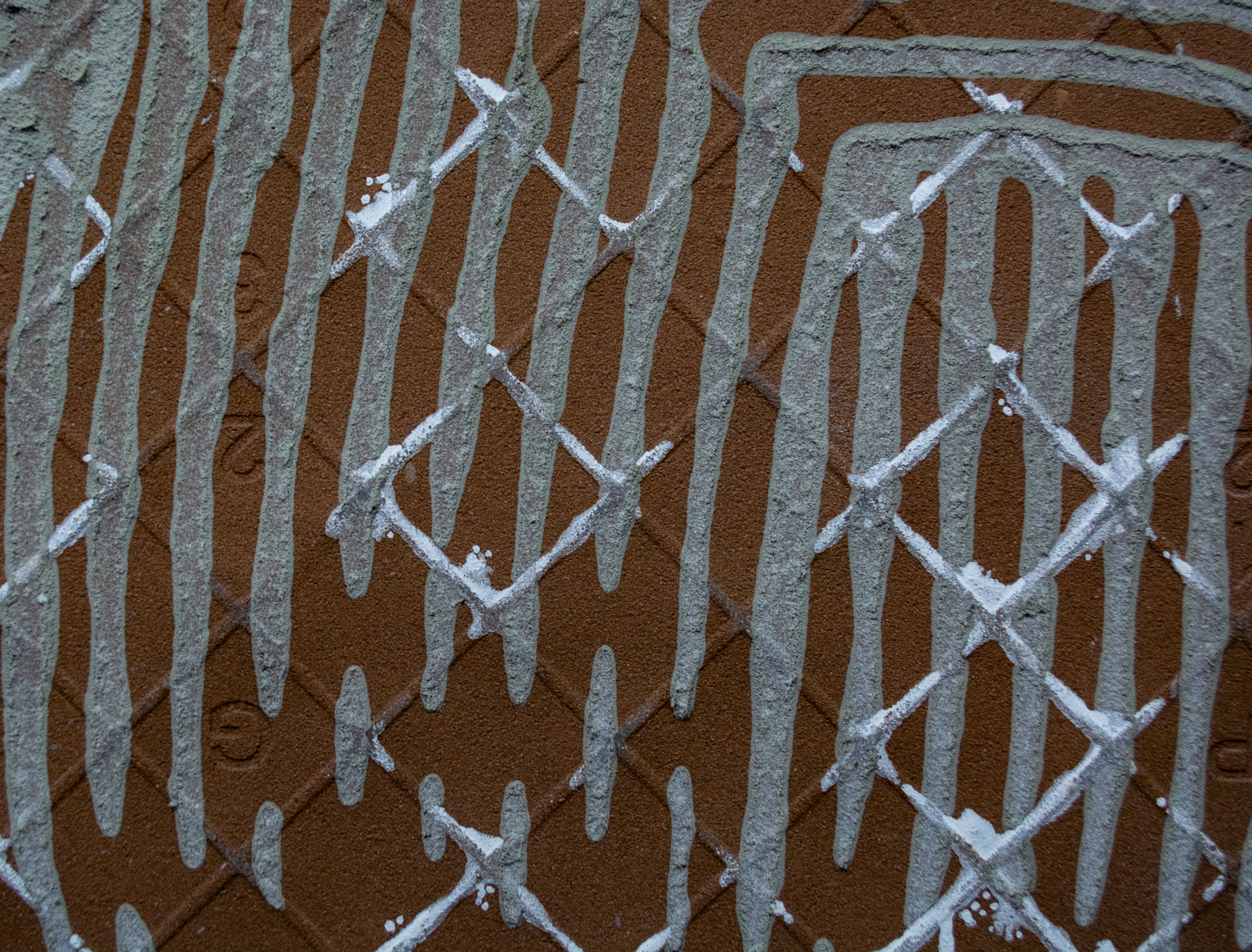 Close-up of white paint dripping in an X-lattice pattern over brown stucco wall