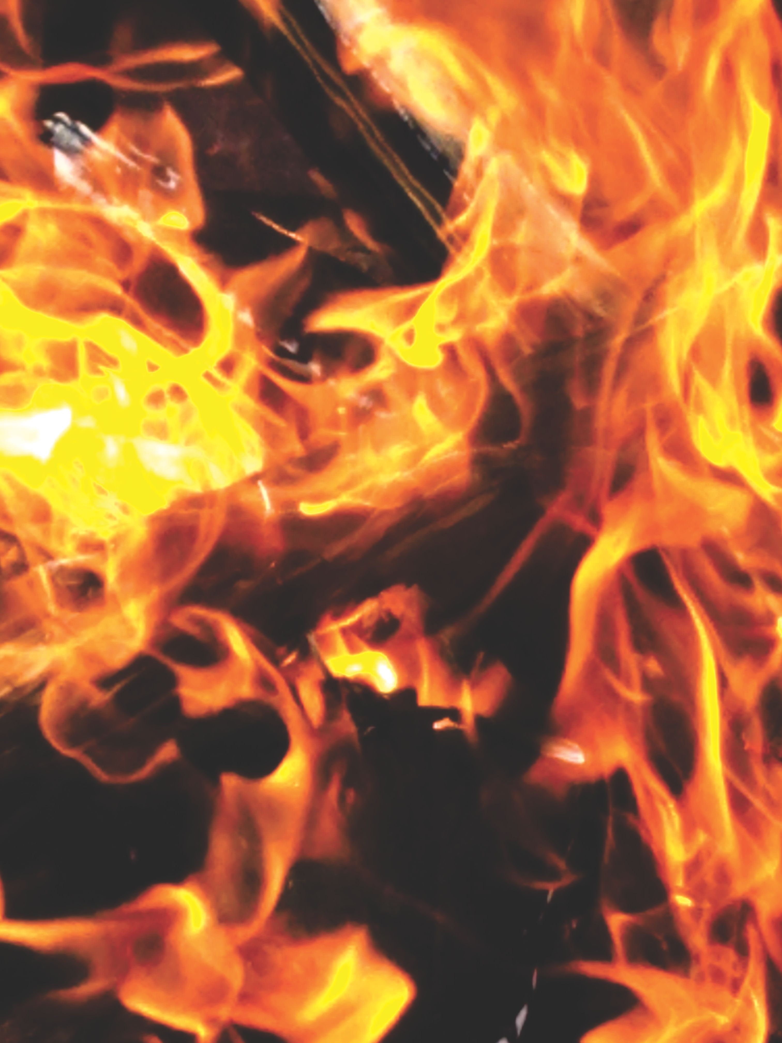 Close-up of bright orange and yellow flames licking over dark charred wood