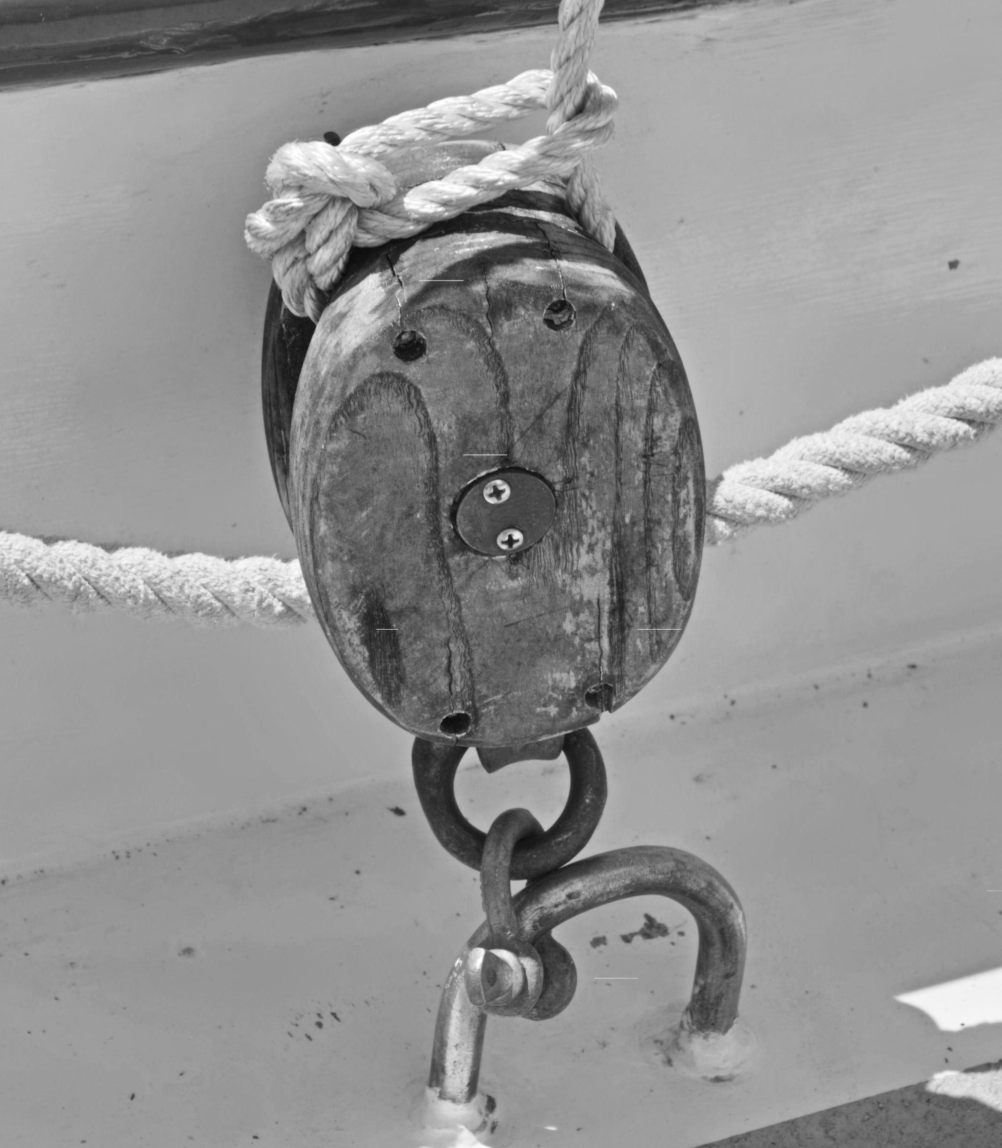 Black-and-white close-up of a weathered wooden ship's pulley wrapped in rope, iron chain and shackle hanging below