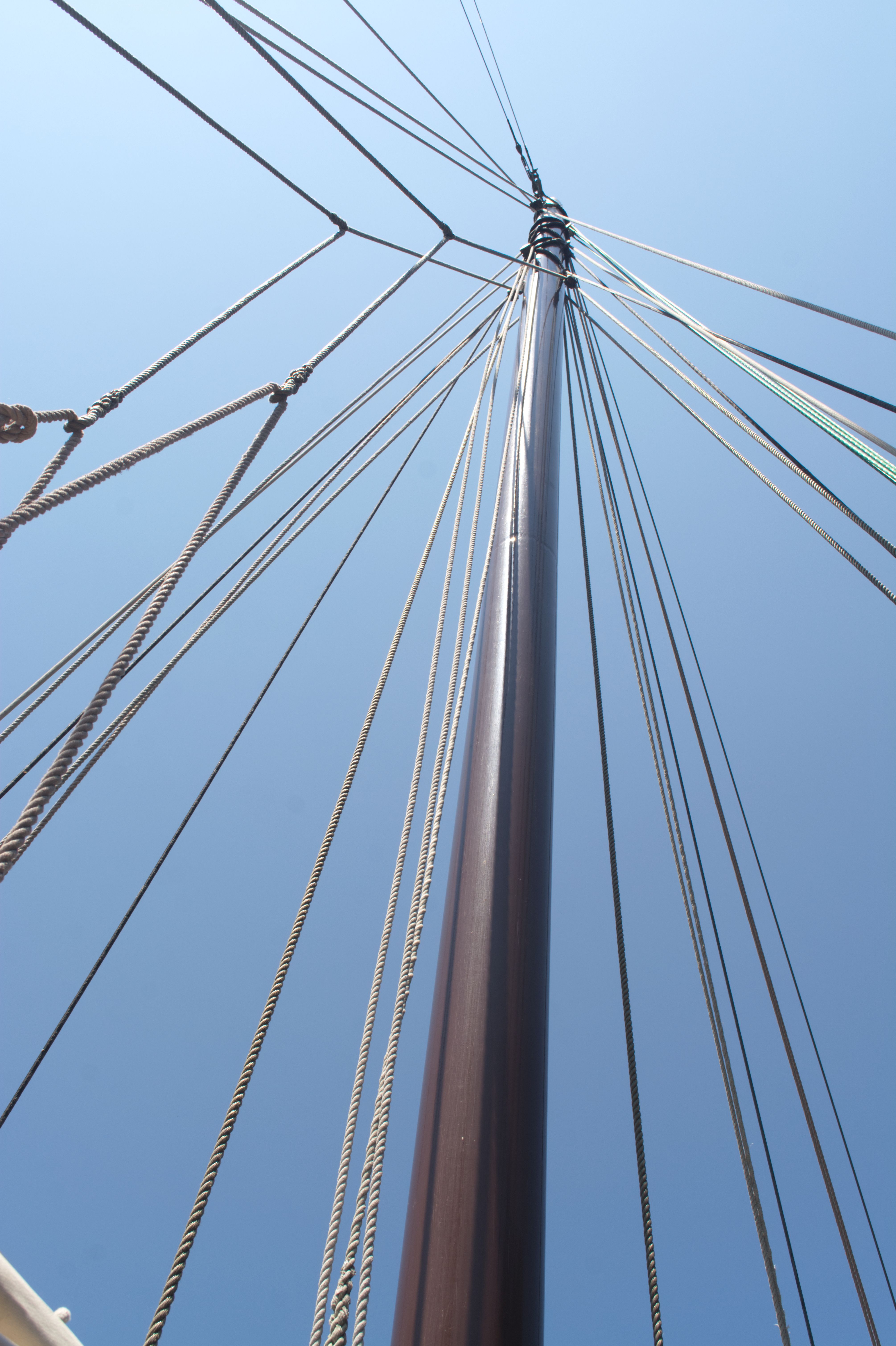 Sailboat mast and rigging lines fanning outward against a clear blue sky, viewed from below