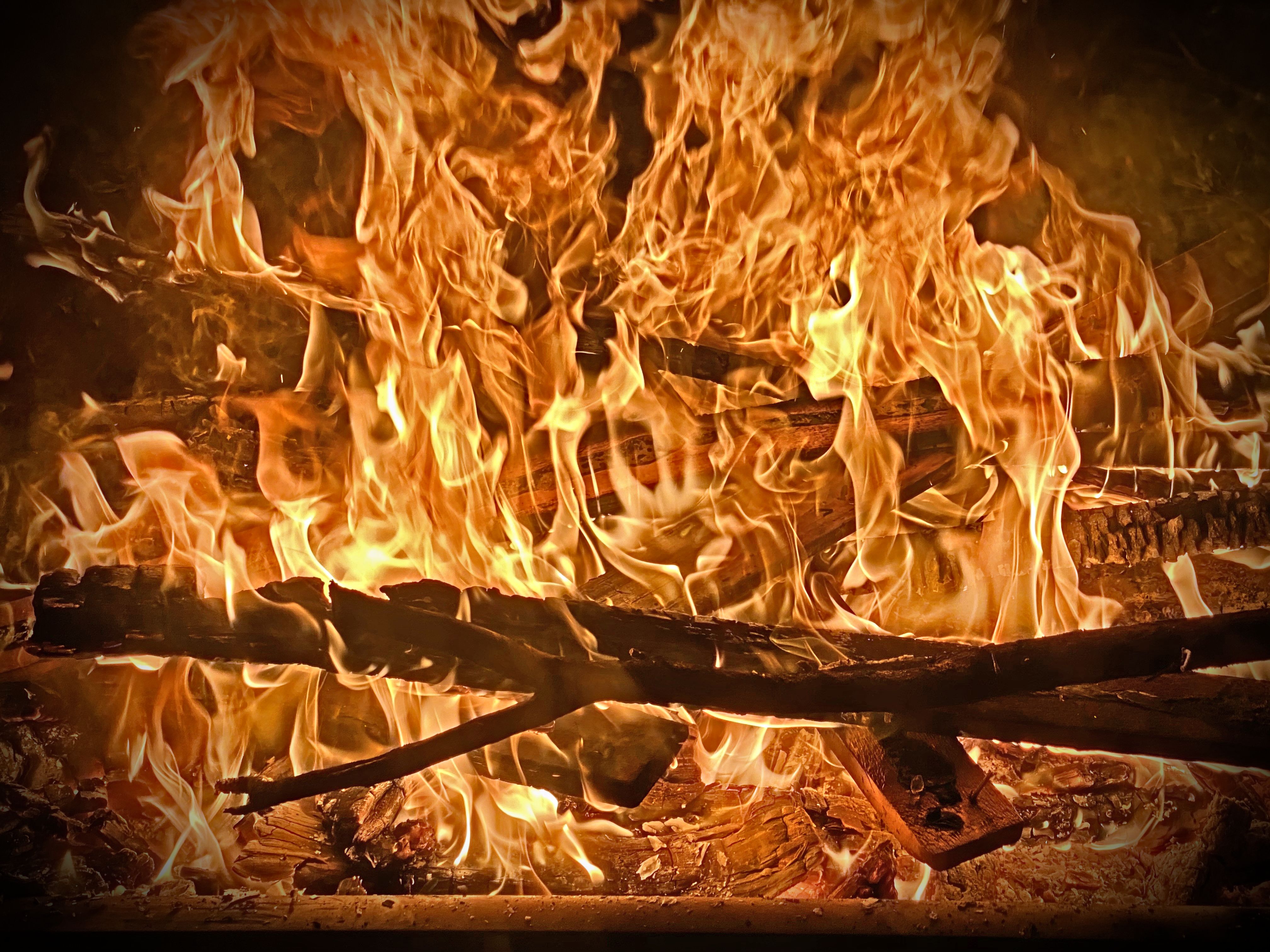 Roaring orange flames engulf crossed logs in a dark fireplace, deep amber glow