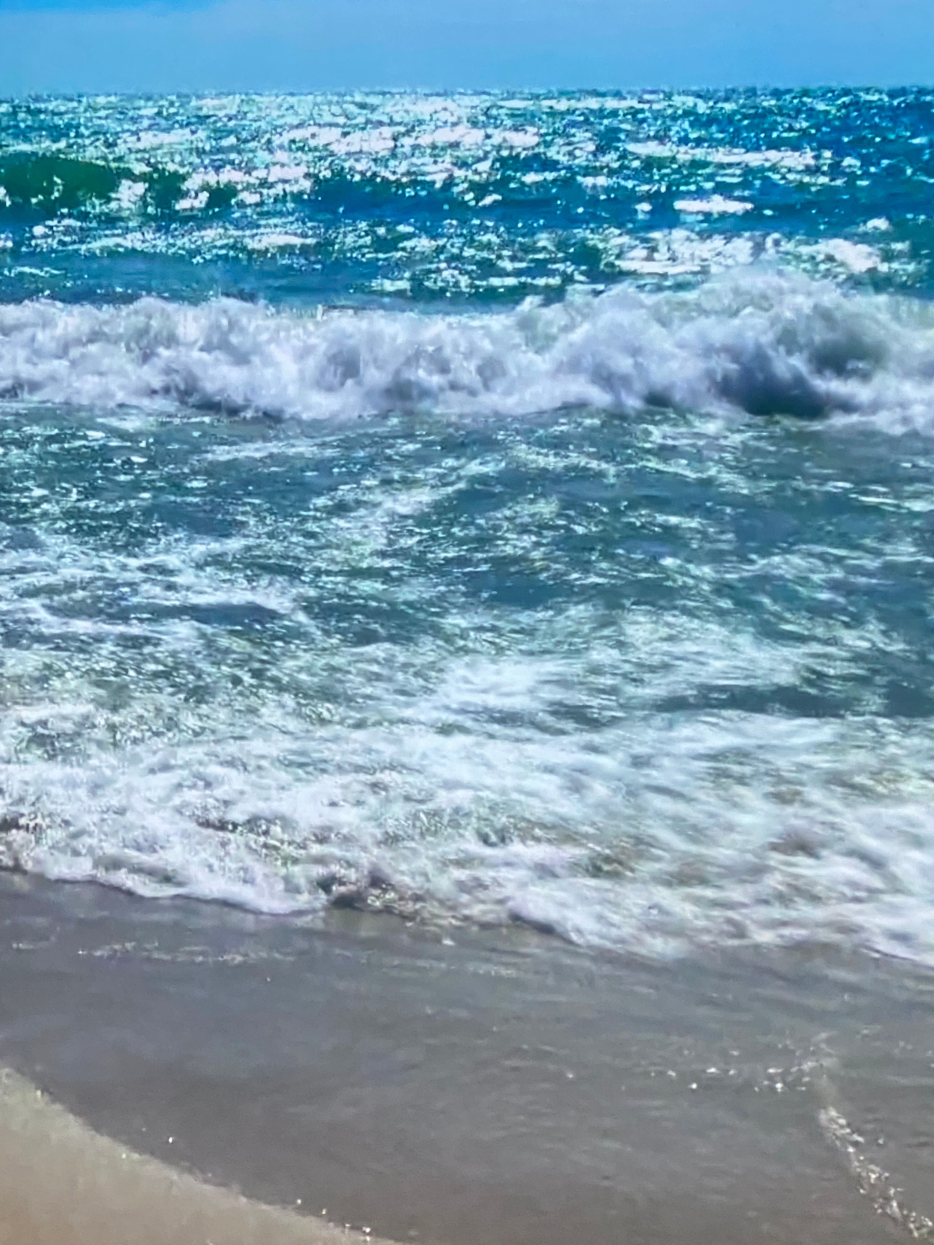 Foamy white wave crashing onto gray sand with teal ocean beyond