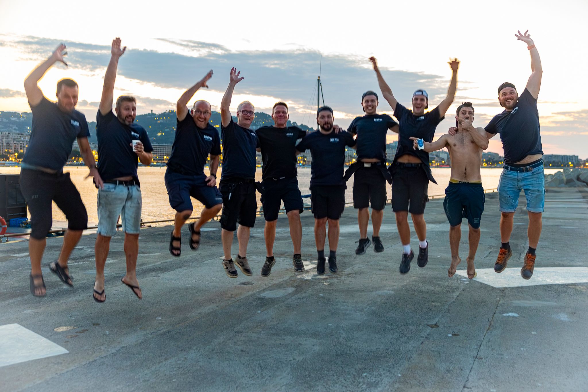 Members of the JoHo Pyro team jumping together on the quay in Cannes at dusk.