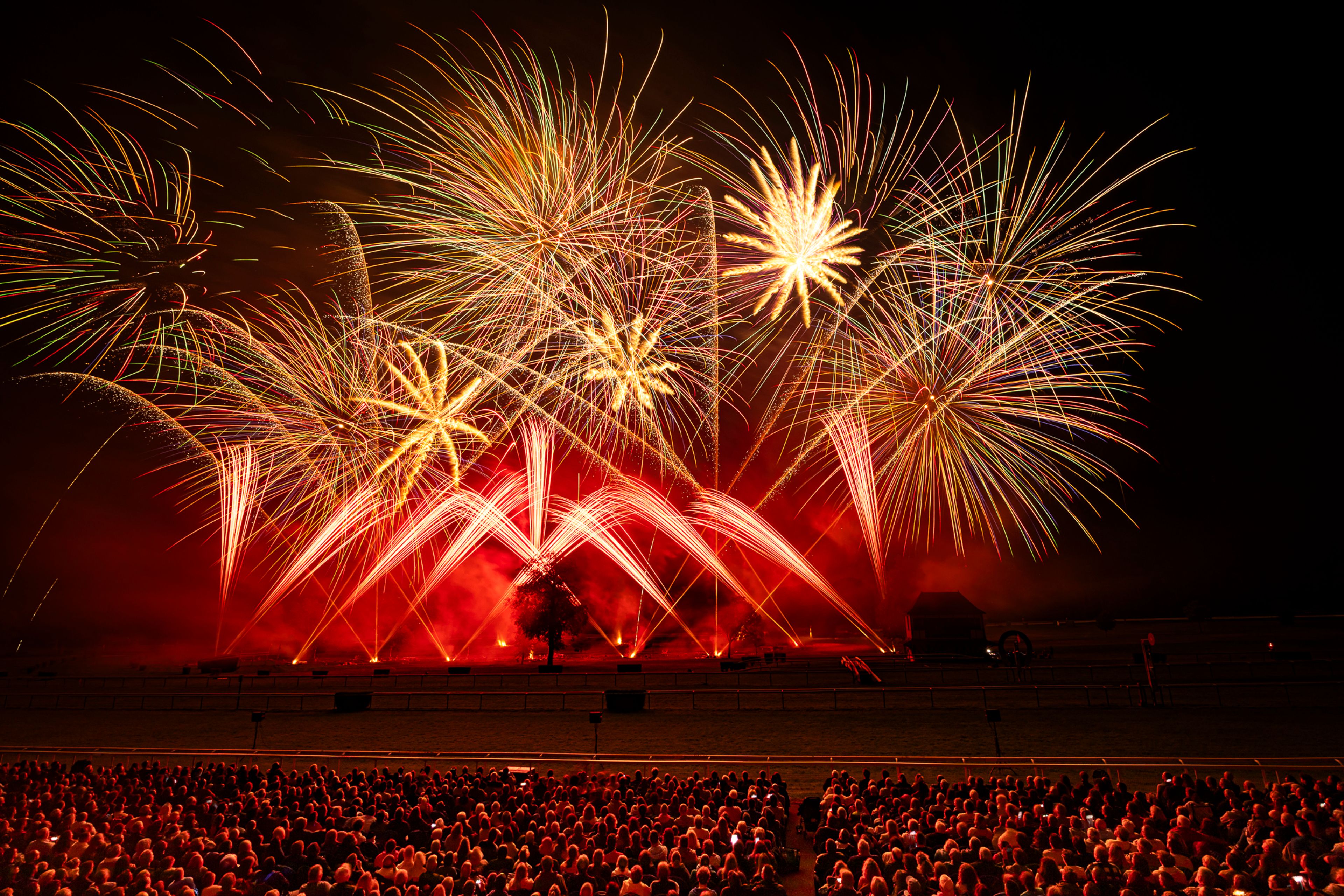 A large crowd watches a fireworks display lighting up the night sky with red, orange, and yellow bursts and arching trails at the Masters de Feu 2024 event in Compiègne, France, on September 21, 2024.