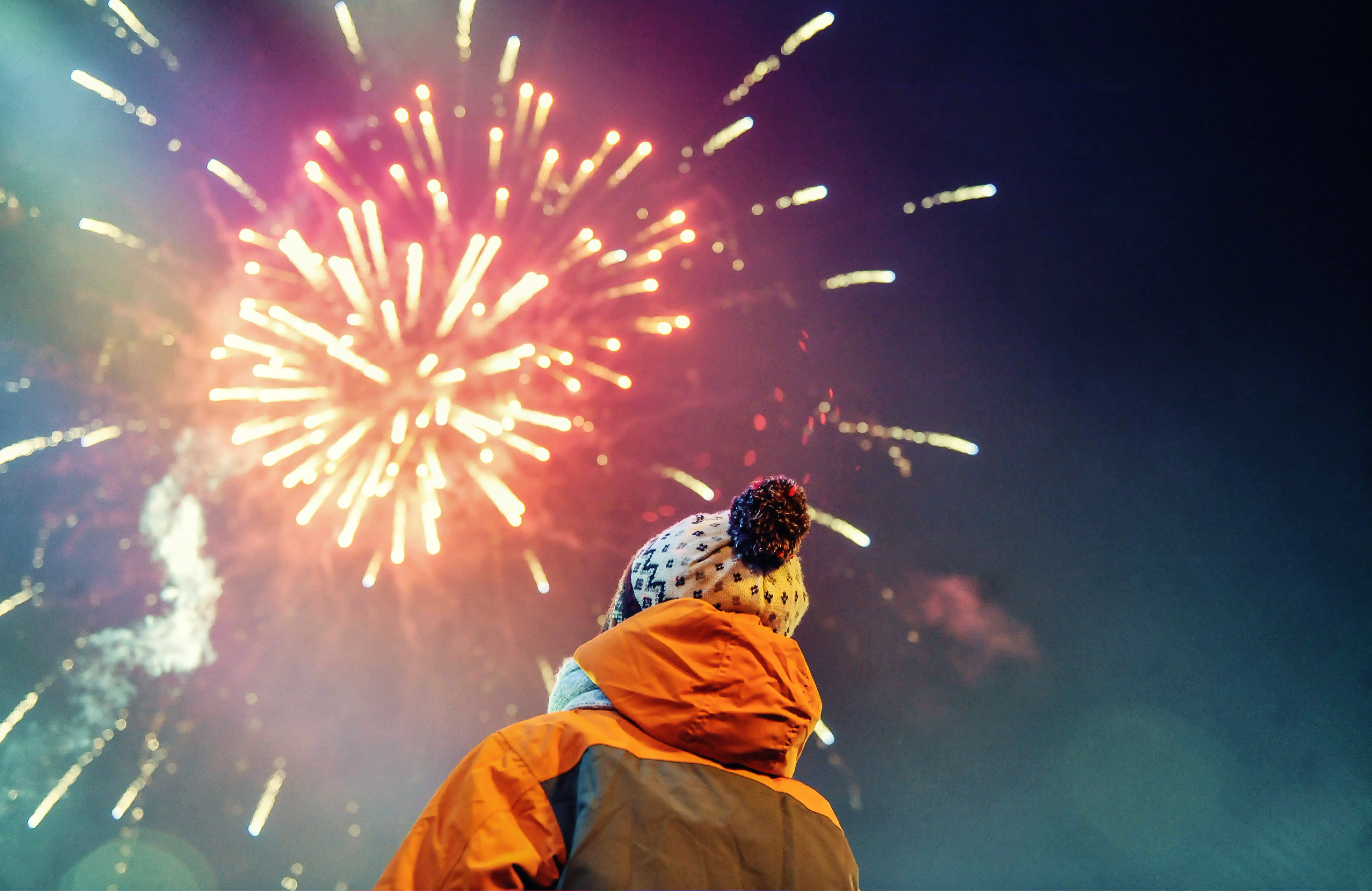 A spectator in an orange jacket watching fireworks.