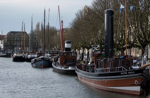 Historic ships moored along the Wolwevershaven quay in Dordrecht with merchant houses behind