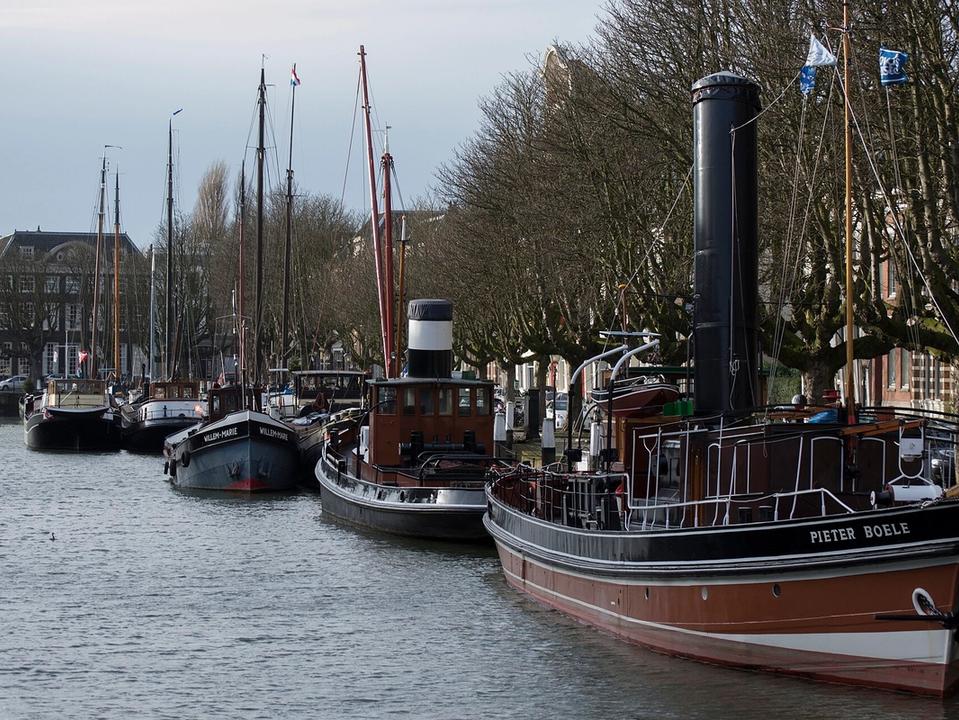 Historic ships moored along the Wolwevershaven quay in Dordrecht with merchant houses behind