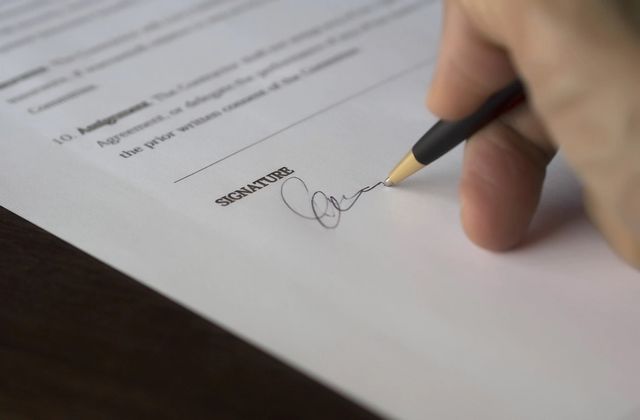 A person signing a Dutch rental contract at the signature line with a pen
