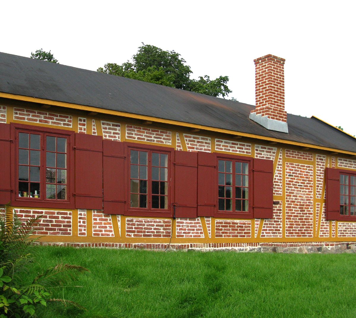 Foto av huset etter rehabilitering. Vinduer er nye, murt rød teglfasade, trekonstruksjon synlig i fasaden er malt gult. 