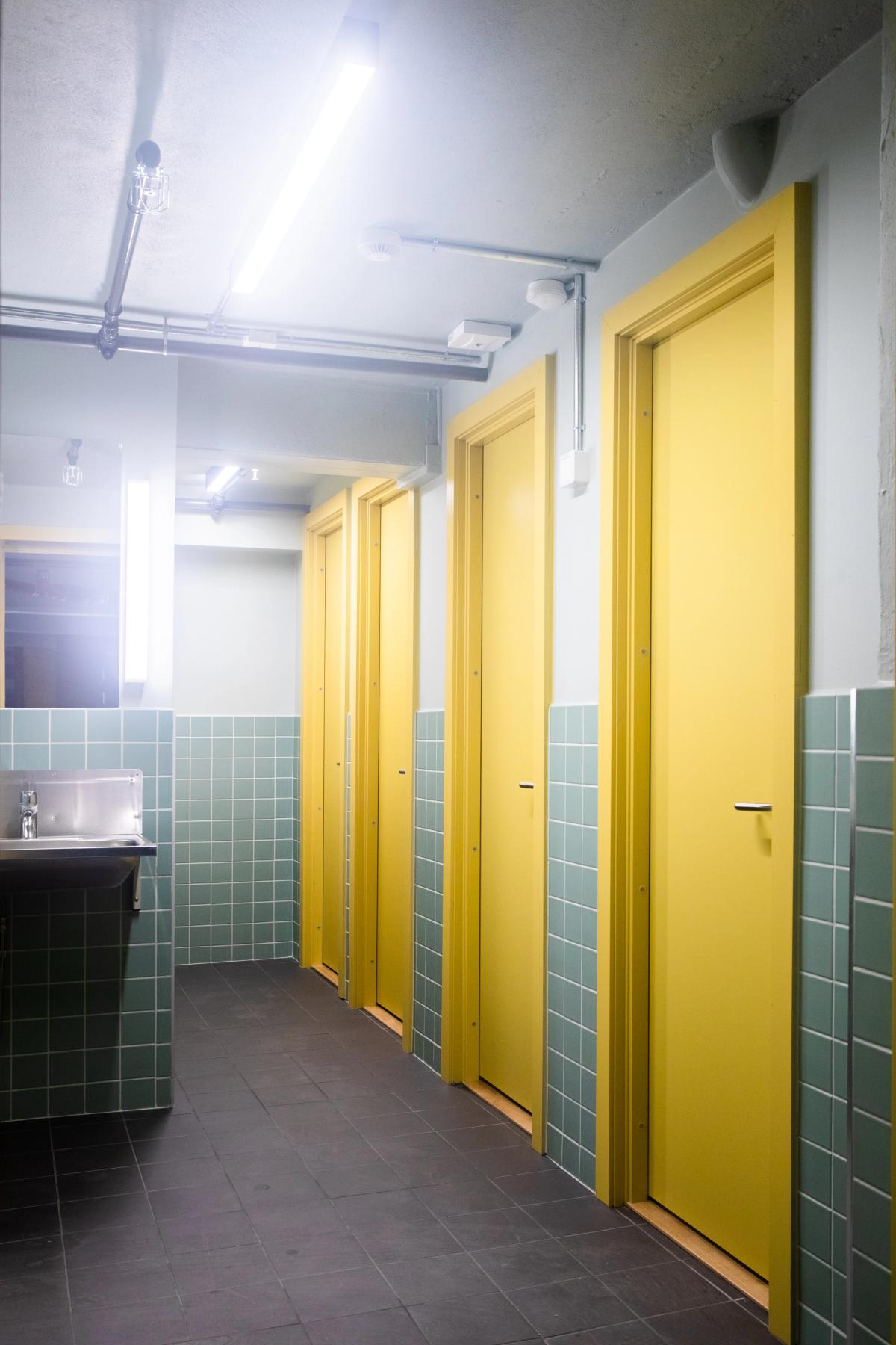 Toaletter i underetasjen, rekke med gule dører og grønn veggflis. 