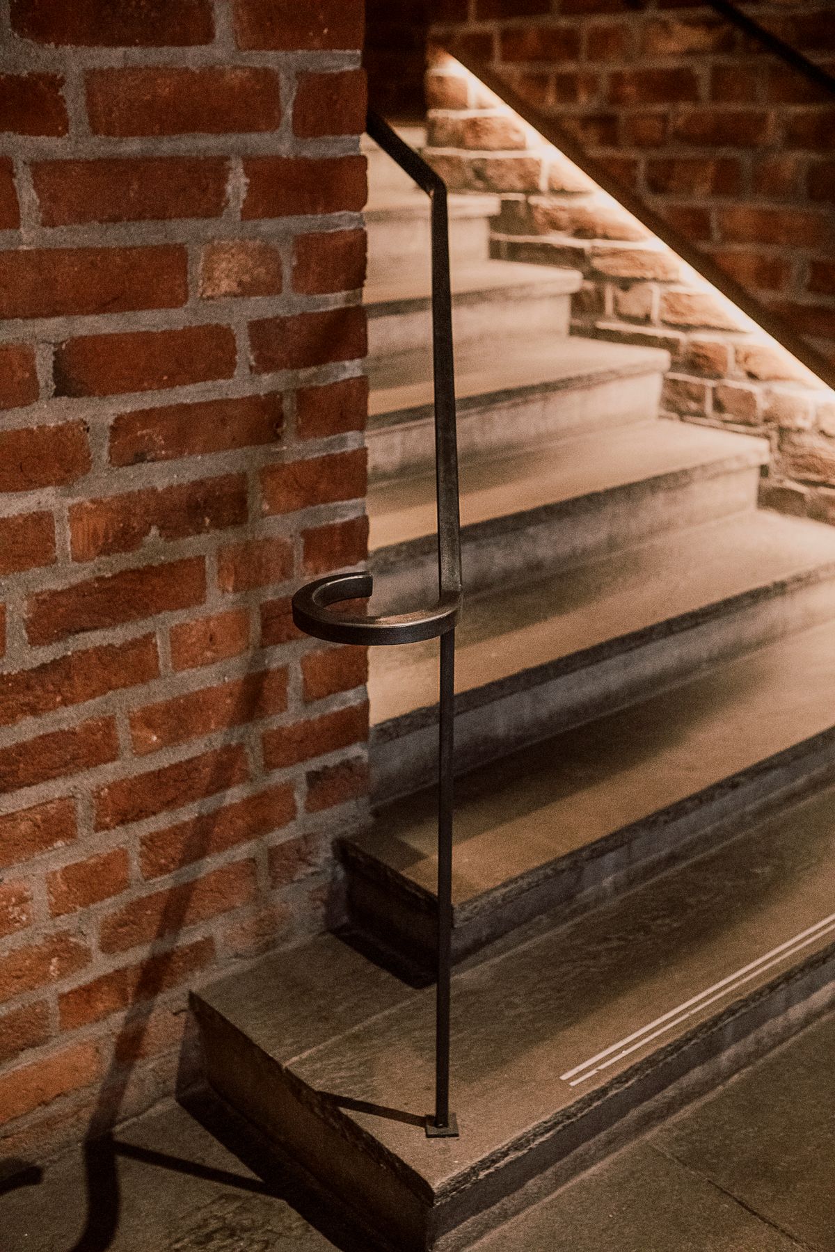 Detaljfoto av belyst trapp for universell utforming og håndløper i sort metall. 