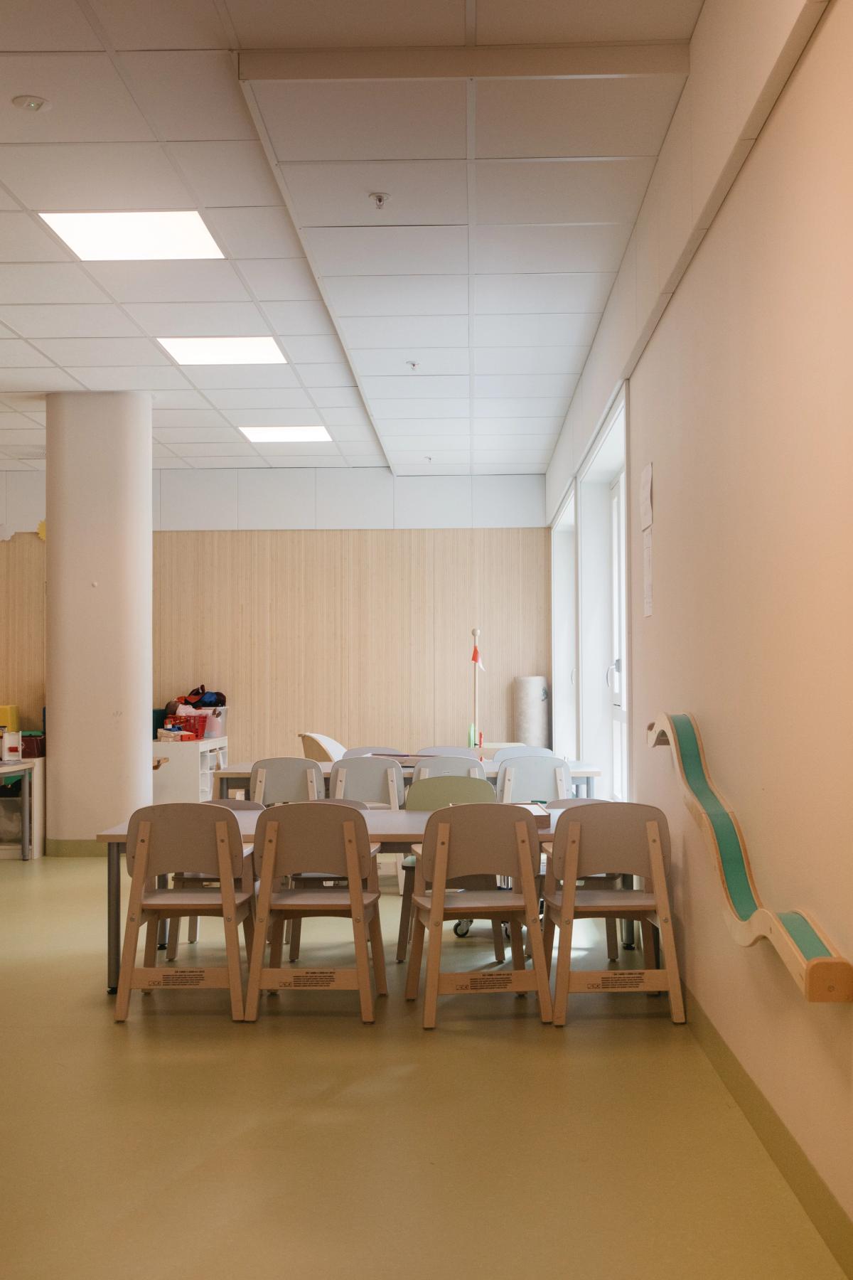 Foto av interiør barnehage. Grønt linoleumsgulv, lyse flater og trespiler på vegg. 