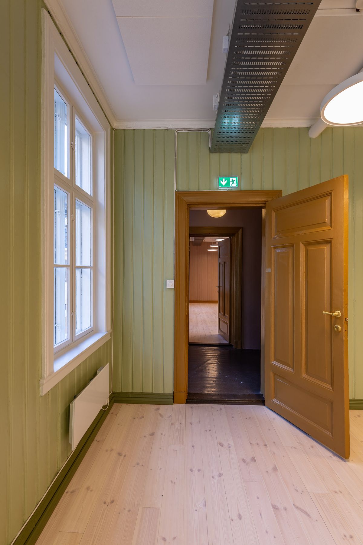 Fotografi av et grønt rom i andre etasje, med perspektiv mot et annet større rom i brune vegger. 