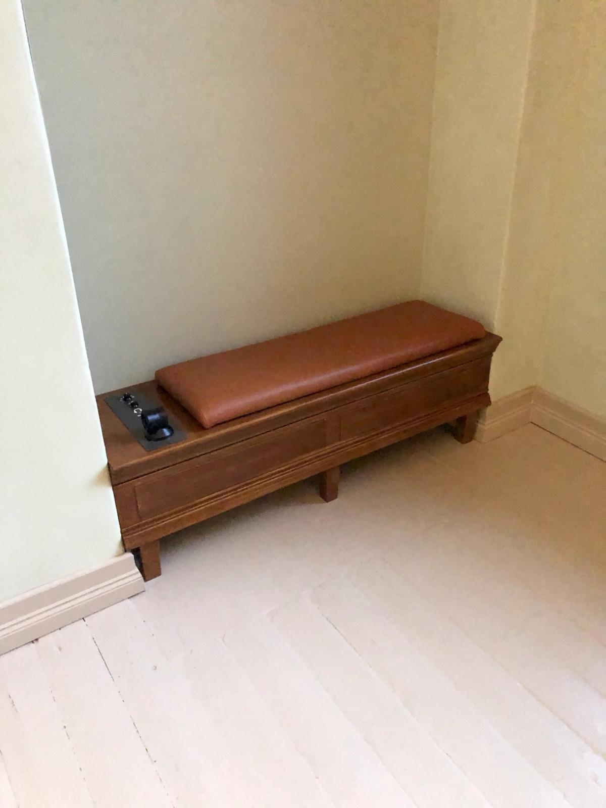 Foto av sittemøbel med integrert høyttaler. Møbelet i mørk tre med lærsete, tilpasset en nisje. 