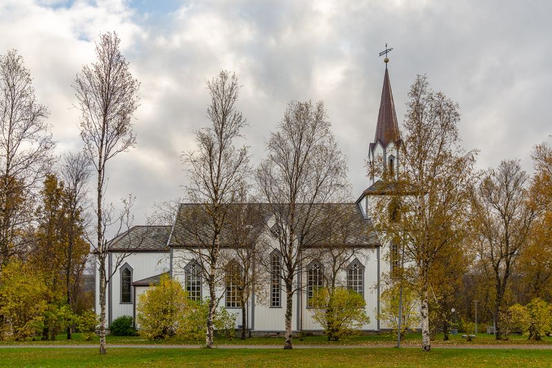 Foto av kirken omringet av høst og trær. 