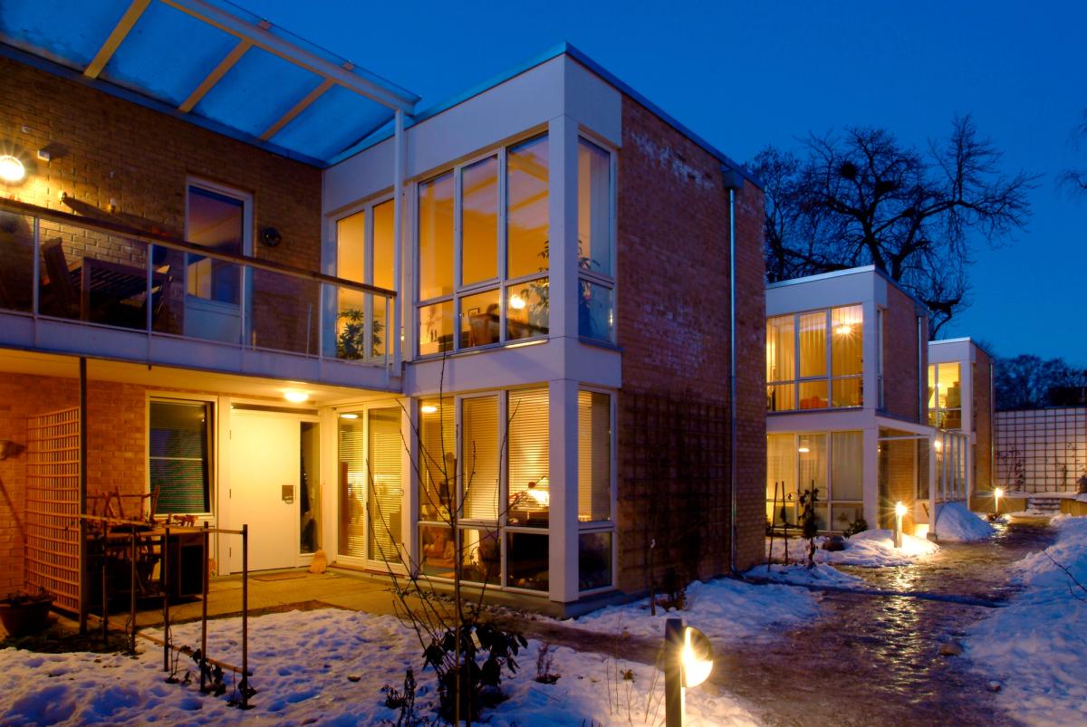 Kveldsfoto av husets 2 etasjer, som viser rød teglfasade og store vindusflater.