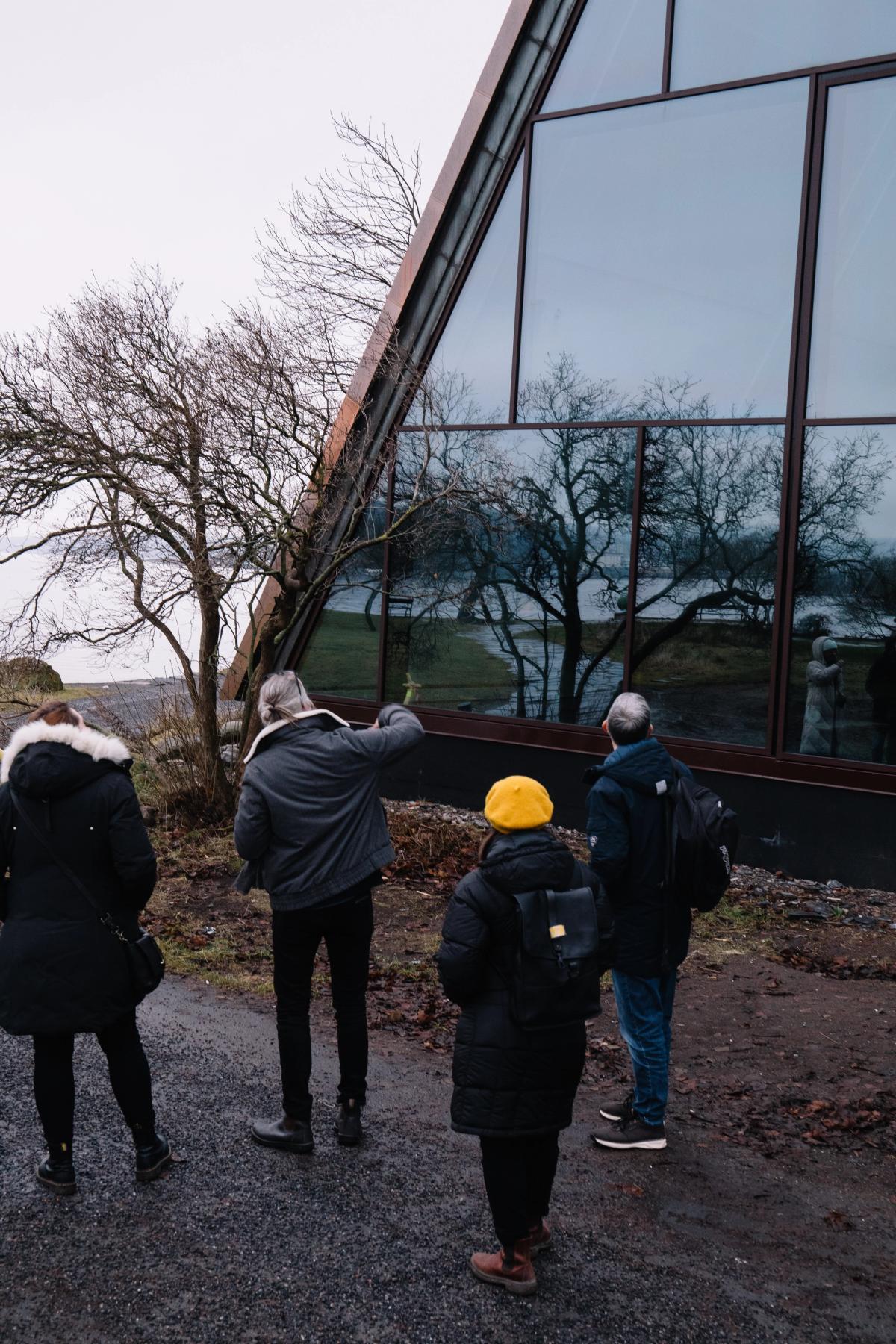 Foto av arkitektgjennomgang. 4 kollegaer står og diskuterer glassfasade og detaljering av tak. 