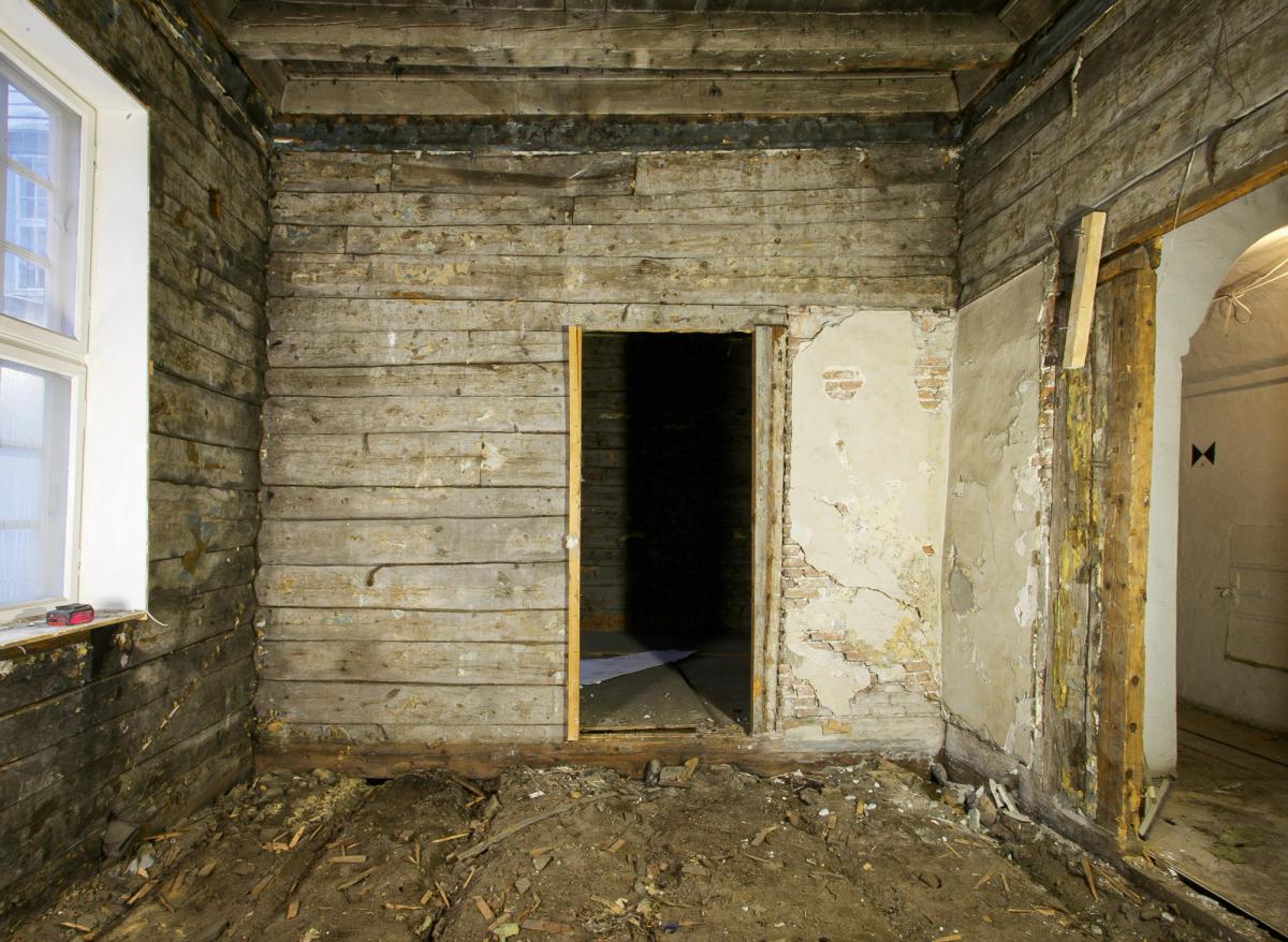 Foto av. rom før rehabilitering, tømmervegger med døråpninger.