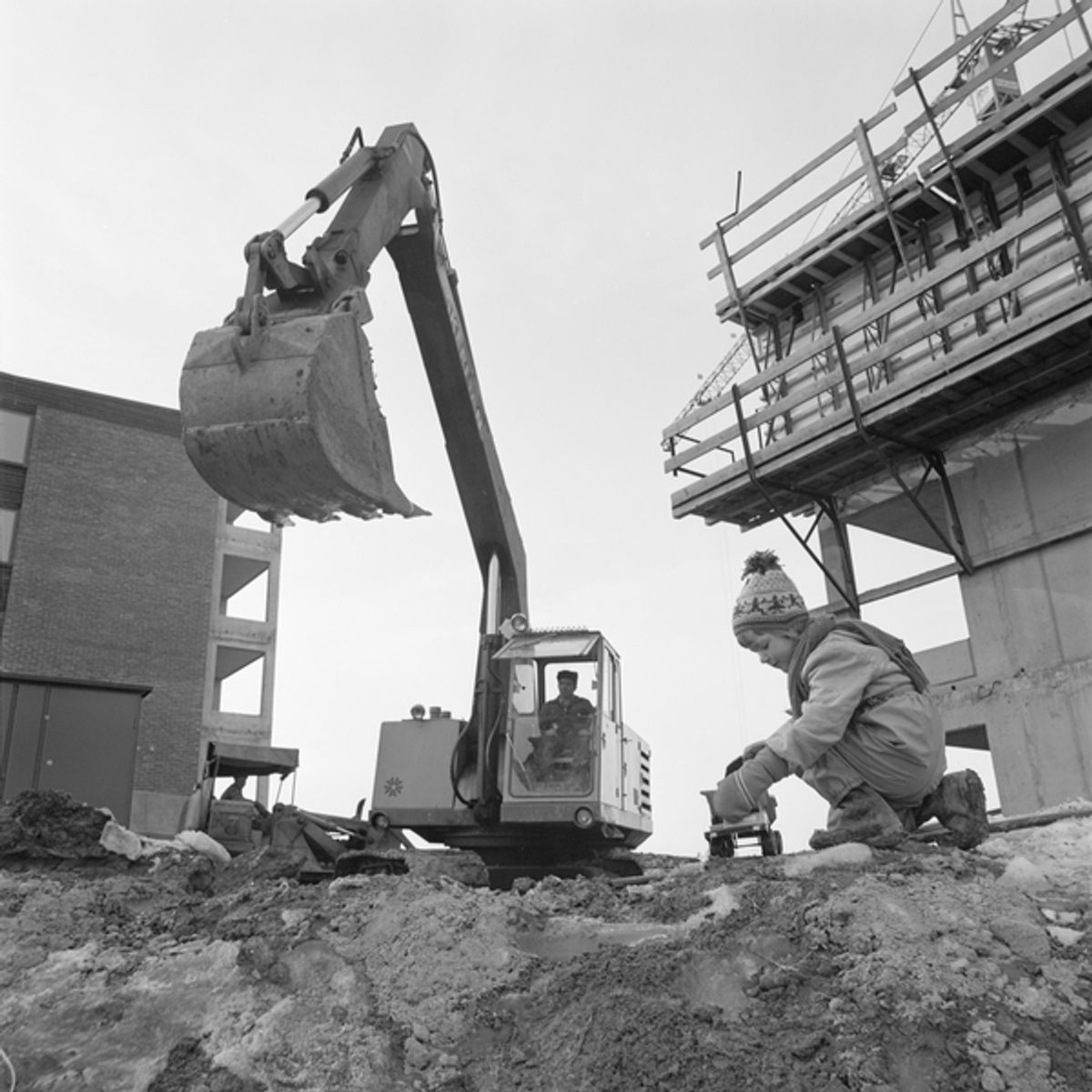 Historisk foto av Hovseterveien under bygging. Foto viser gravemaskin og et barn som leker med en lekebil. Foto er fra 70-tallet og hentet fra Oslobilder.no