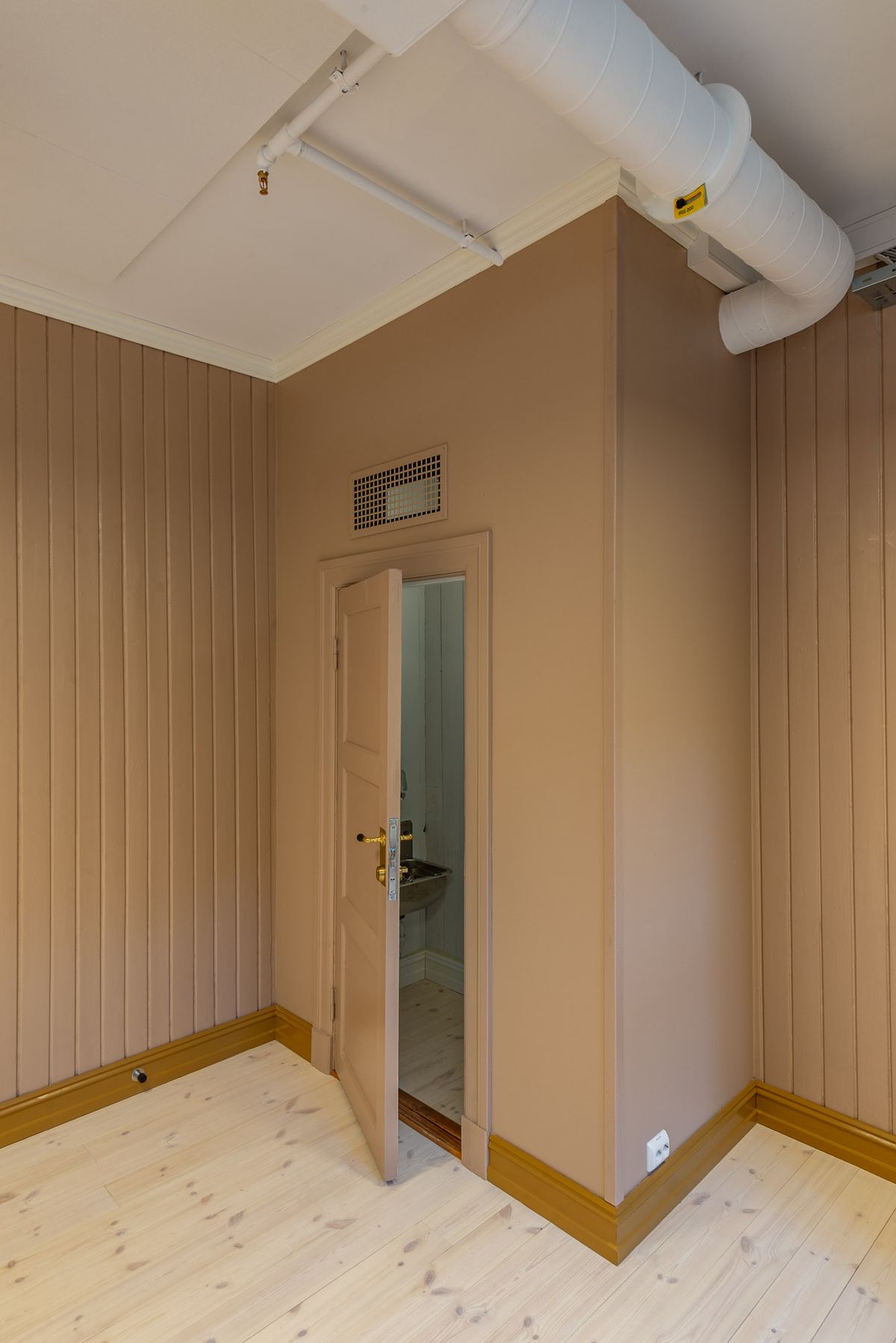 Fotografi av et stort rom i andre etasje med beige vegger og oker/brune detaljer. 
