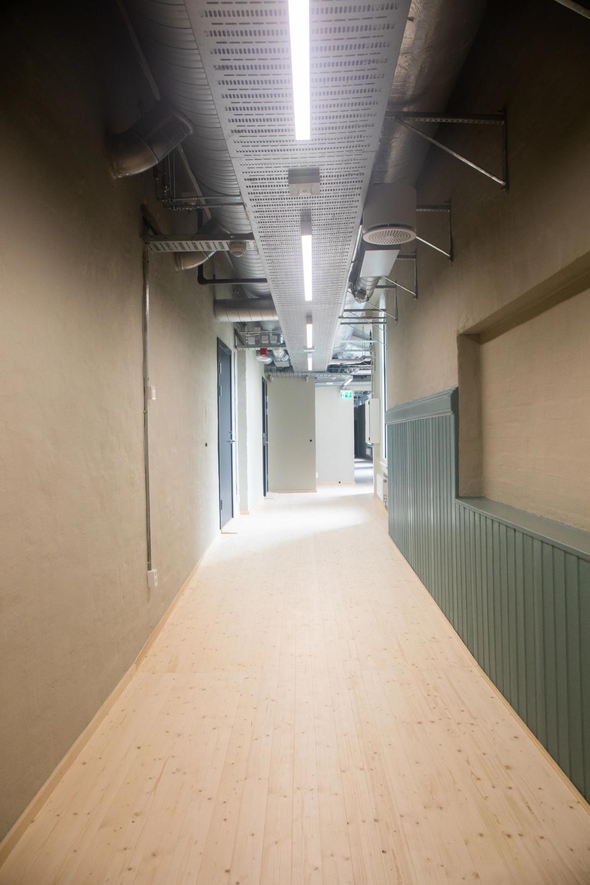 Foto av oppusset korridor med originalt tregulv. Brystning i blått og vegger i beige. 