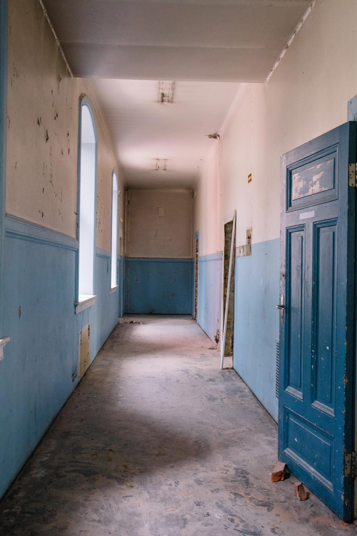 Foto før byggearbeid av korridor, malte vegger, blå brytning og dører.