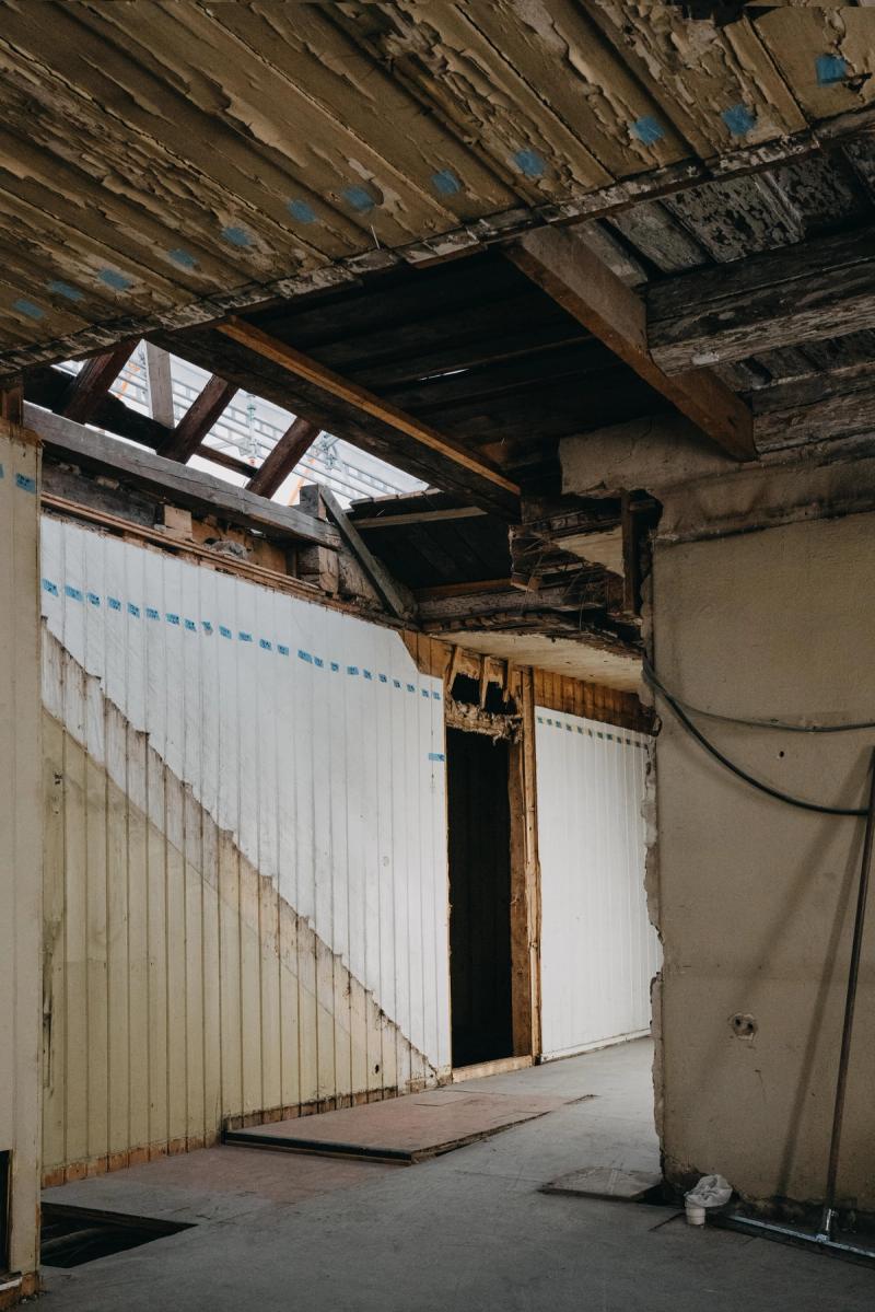 Fotografiet viser interiøret i bygget. Tilstanden er nedstrippet materialer, synlige veggpanel, synlige bjelker og en døråpning. 