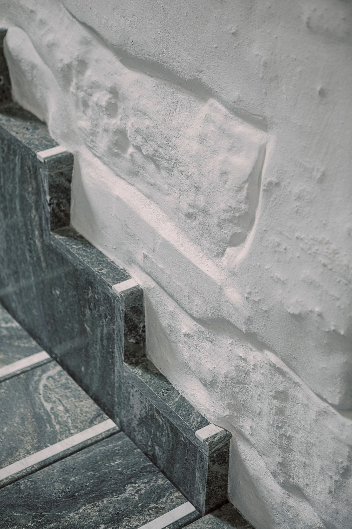 Detaljfoto av trapp i kirkeinngang, møtet mellom trapp og innside pusset teglvegg når trappen er helt nede. 