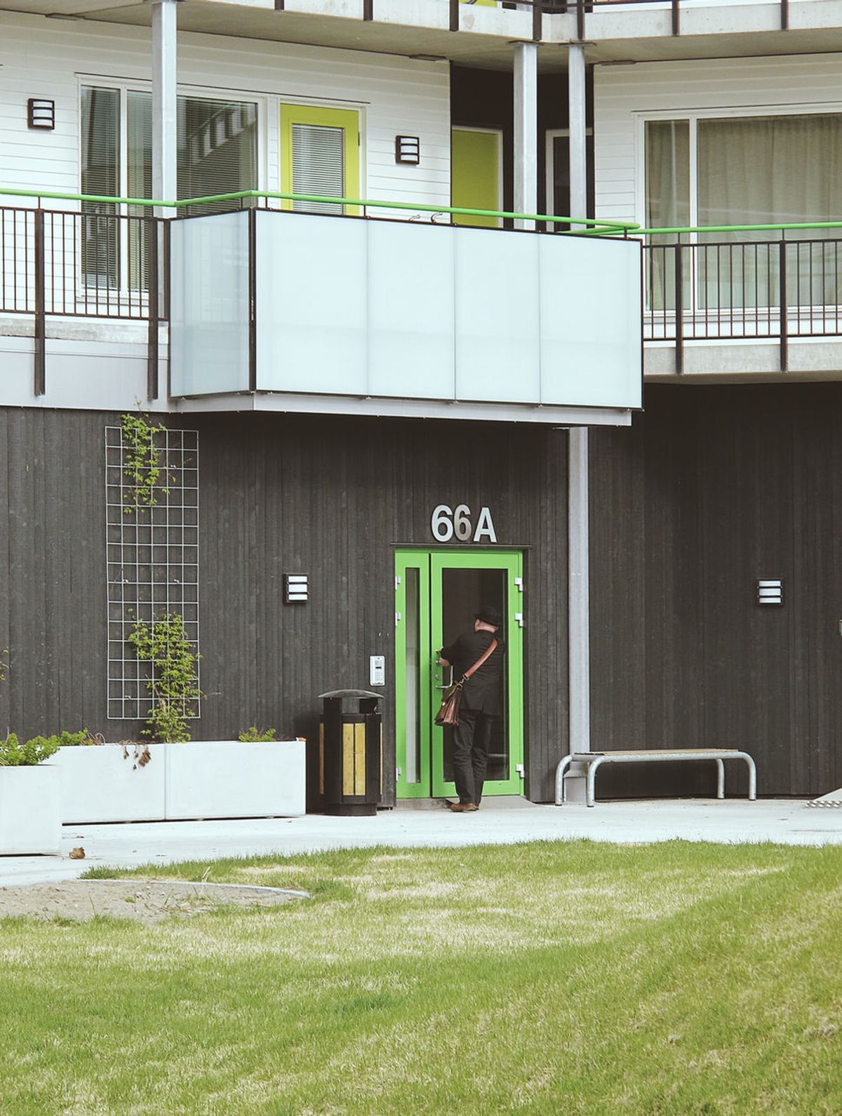 Foto av bakgård. En mann ved grønn inngangsdør. Fasade i hvit og sort trekledning i vertikal og horisontal format.
