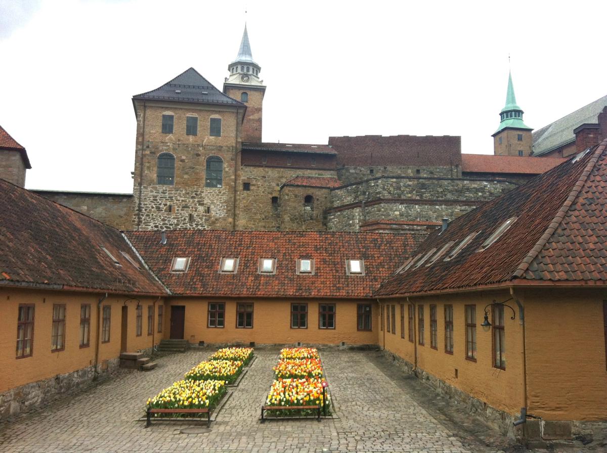 Oversiktsfoto av bygning 3, viser flott gul fasade med tulipaner i seks bed. Akershus slott er i bakgrunnen i bildet.