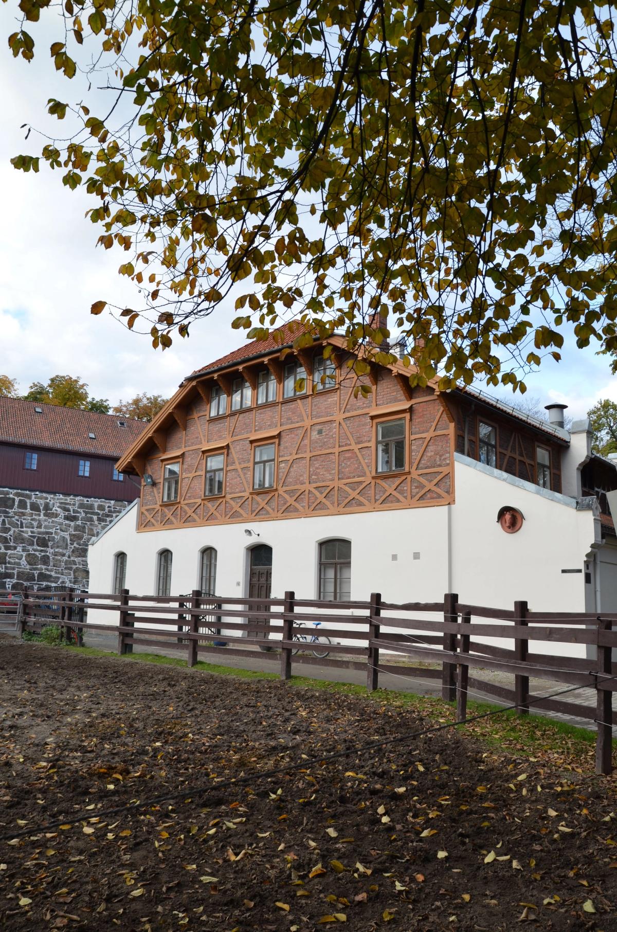 Foto av huset med fasade i hvit puss og rødtegl og synlig trekonstruksjon.
