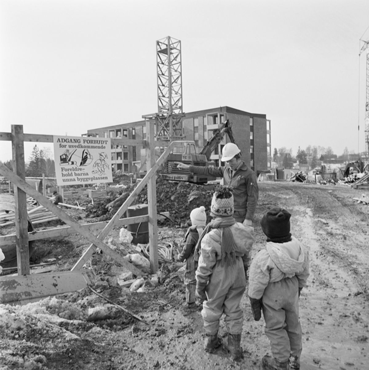 Historisk fotografi av byggeplassen som viser en arbeider som snakker med 3 barn.