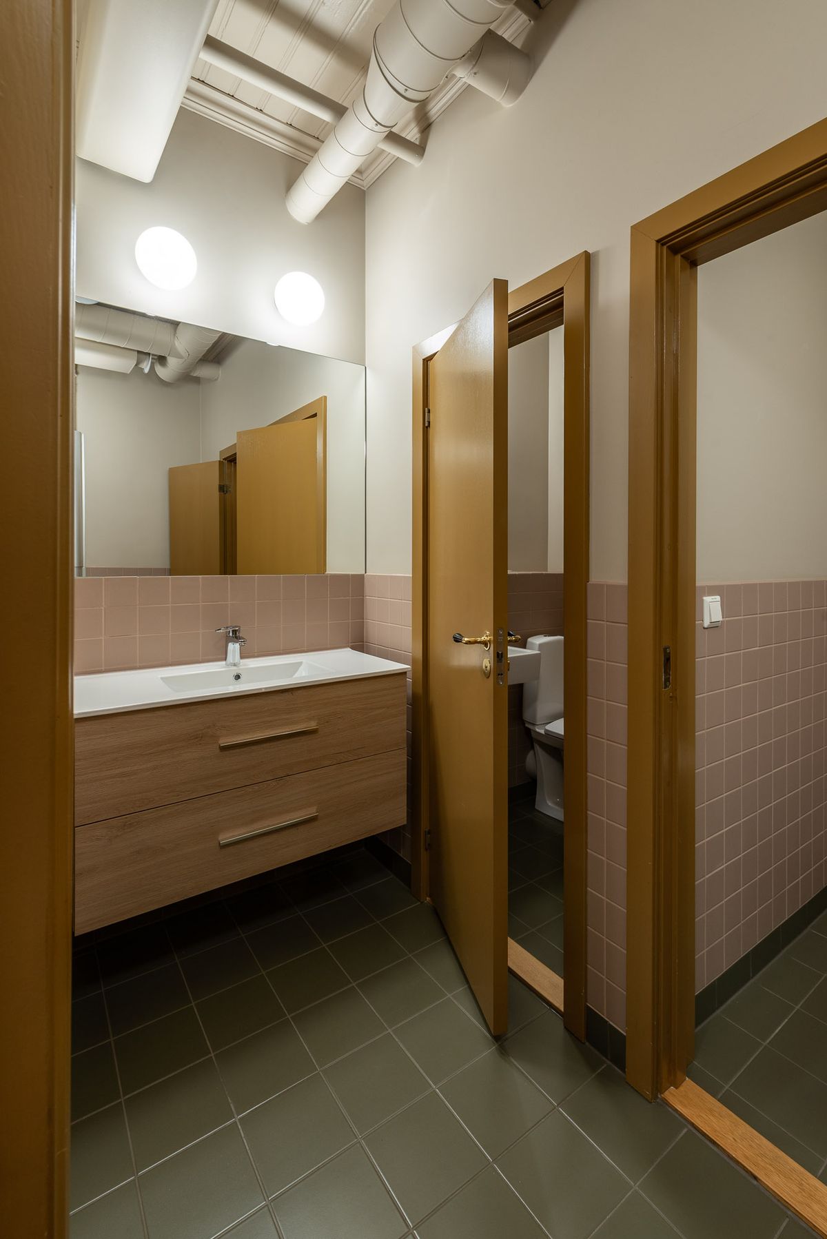 Fotografi av nye toaletter, grønn flis på gulv, rosa flis på halv vegg og oker dører.