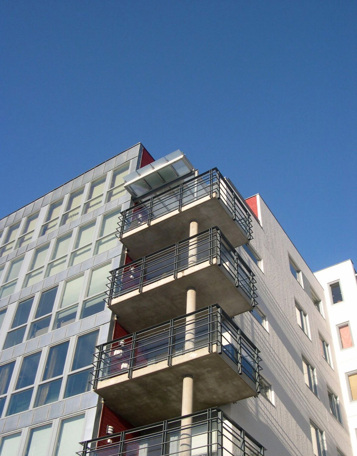 Detaljfoto av bygget som viser lys fasade og glassbalkonger under en blå himmel.