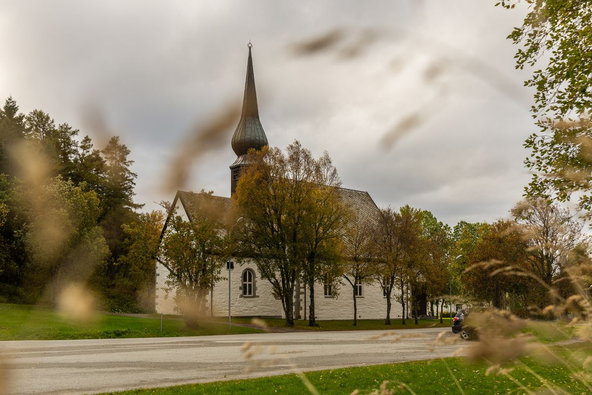 Foto av kirkens gårdsplass en høstdag. Kirken mellom landskapet. 