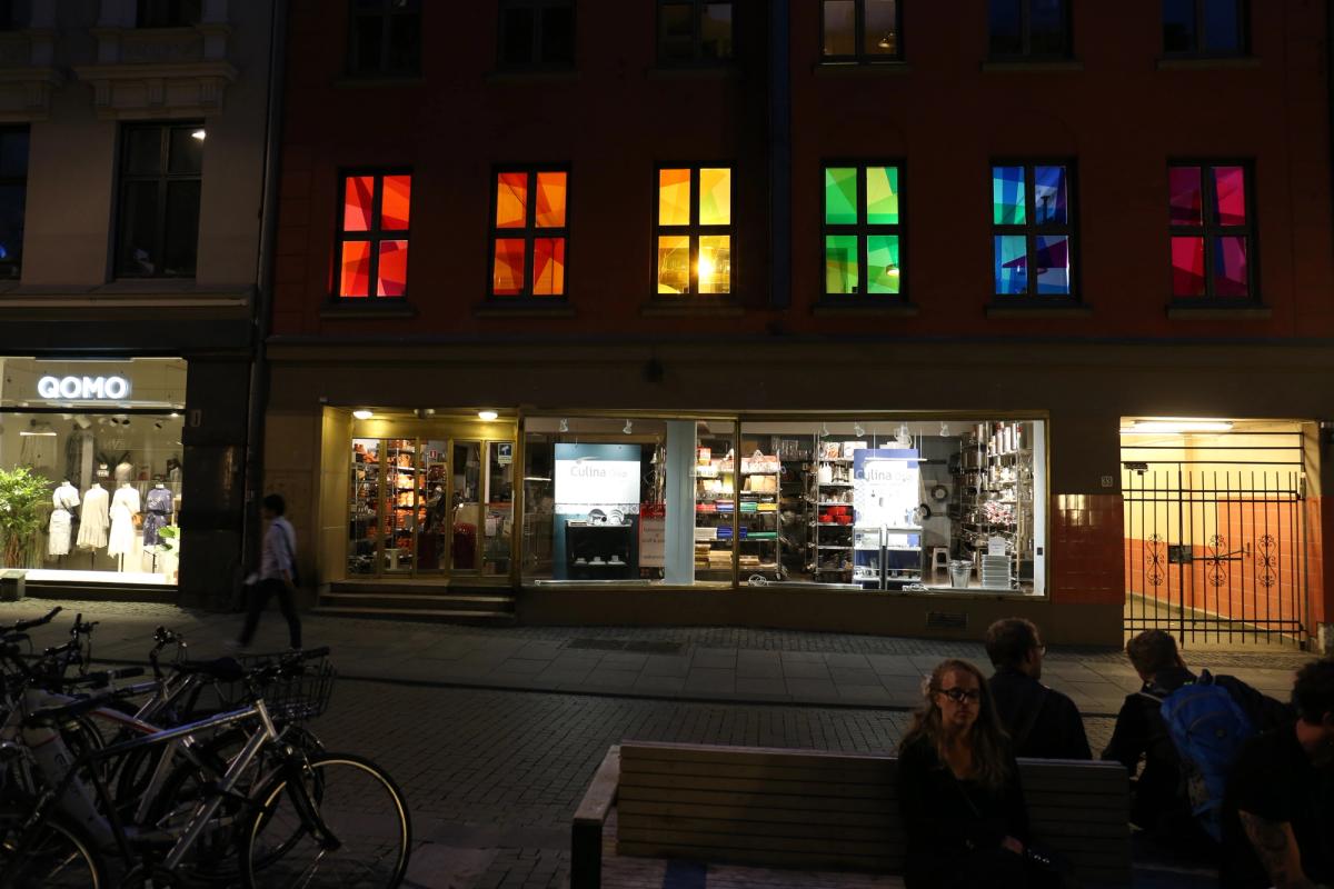 Regnbueinstallasjon i seks vinduer. Foto er tatt utenfra på kveldstid.