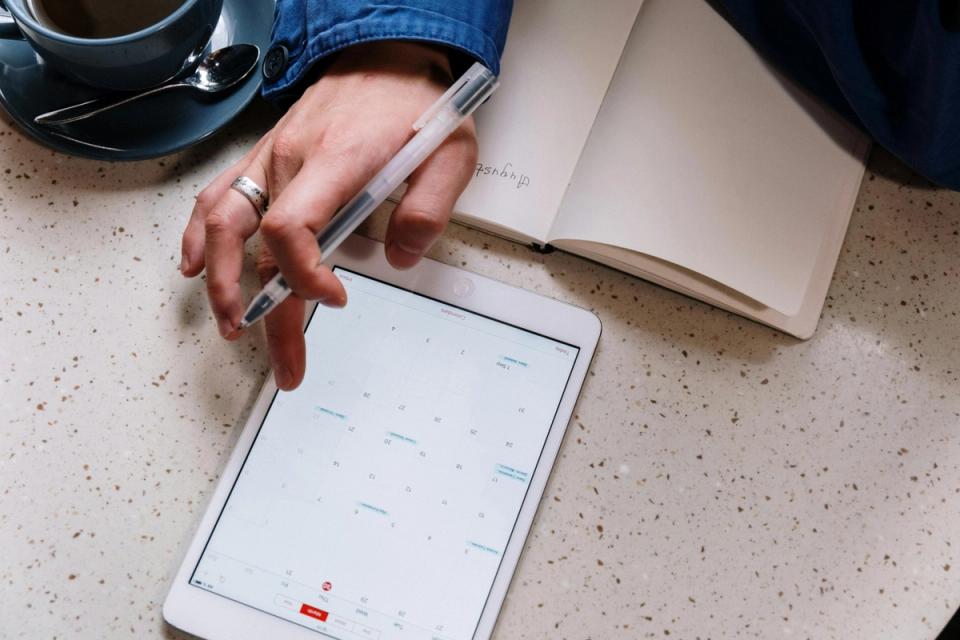 Person using a tablet with notebook on a desk while reviewing home tasks