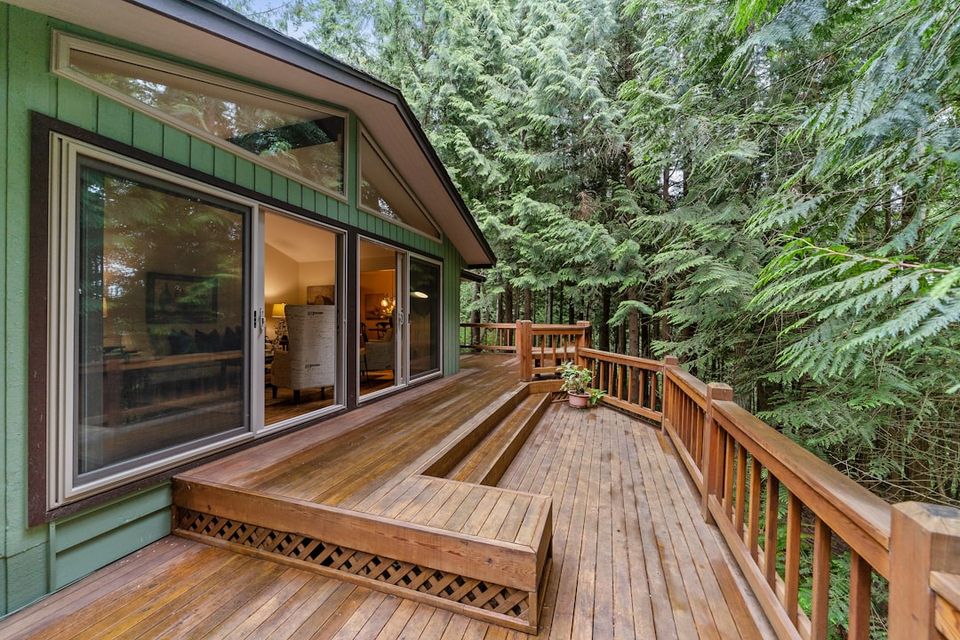 Residential wood deck with railings attached to a green house, showing the outdoor deck inspection step of a summer home maintenance checklist