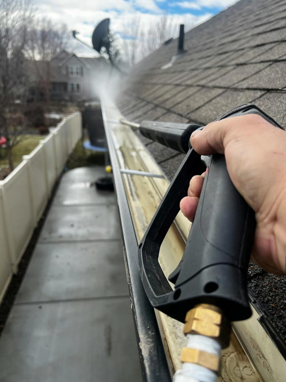Homeowner pressure-washing a residential roof gutter with a hose gun during spring cleanup